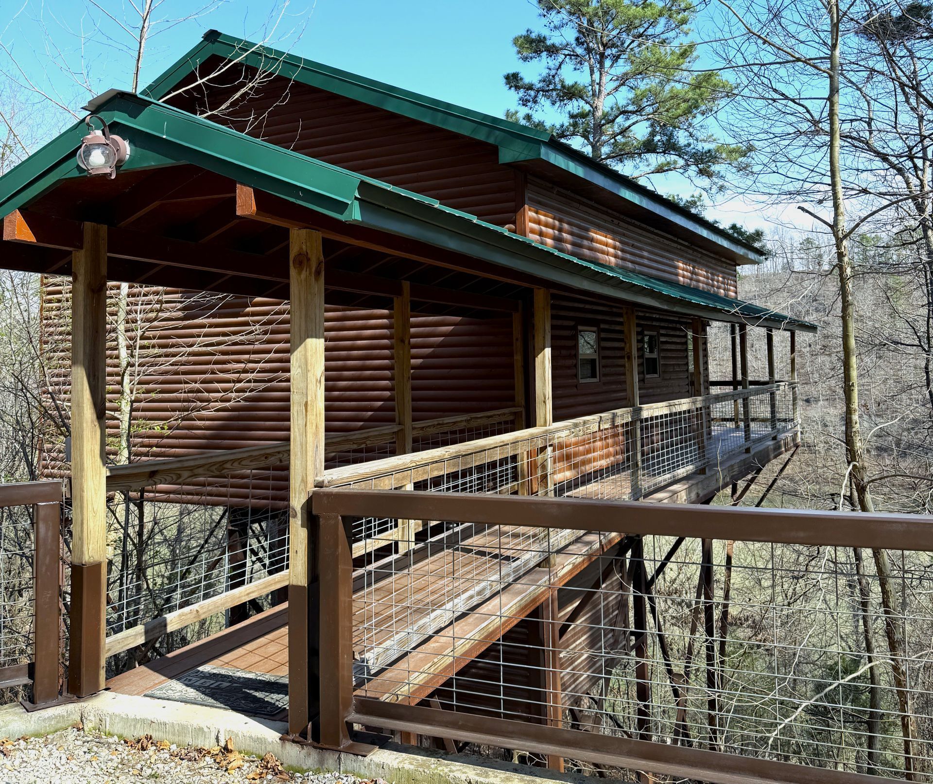 Wooden cabin with green roof and porch on a raised deck in a wooded area