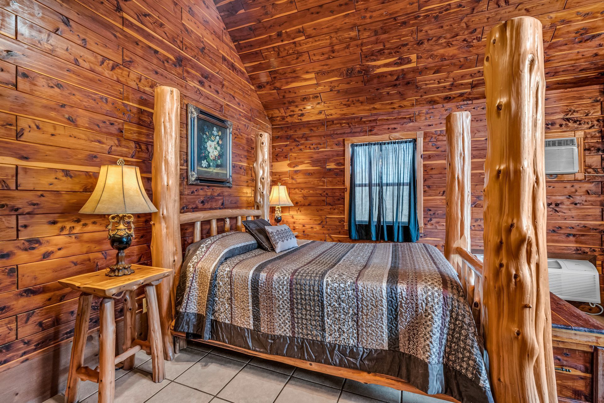 Rustic log cabin bedroom with a wooden bed, lamp, window, and warm wood-paneled walls