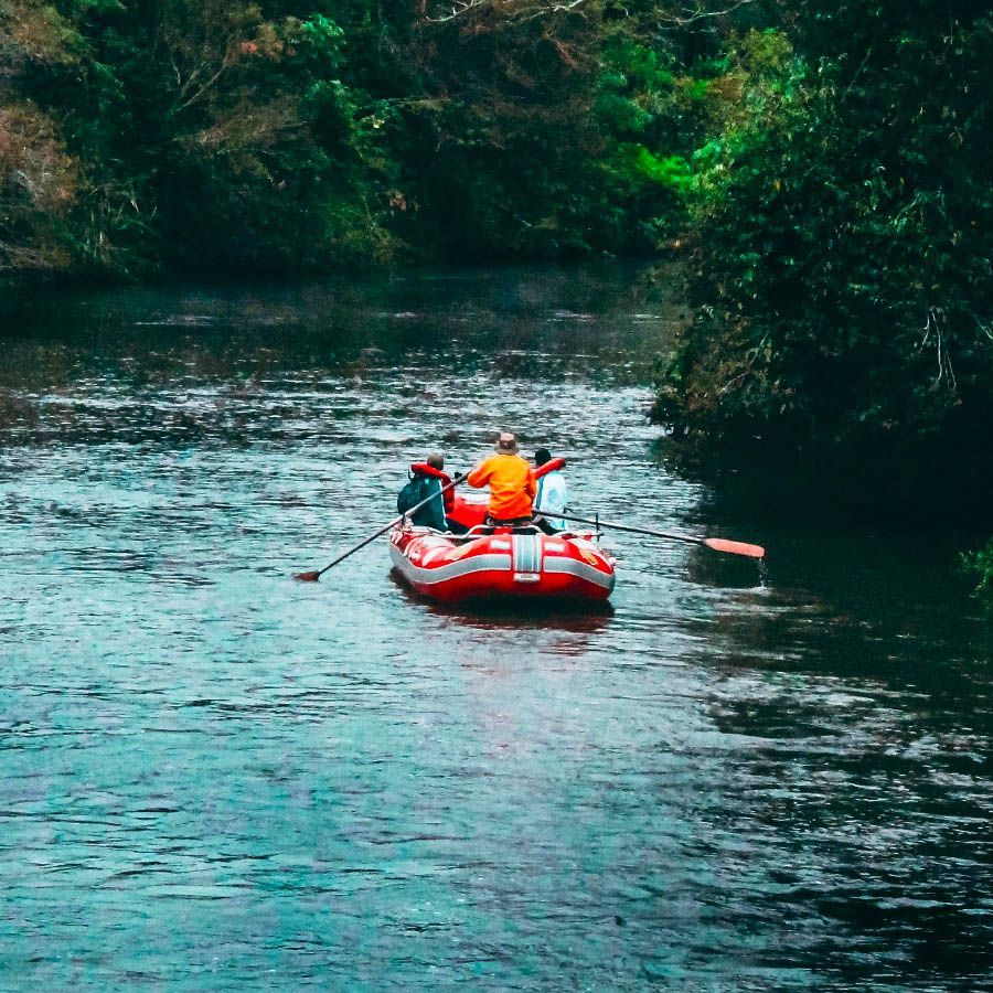 Two people in a red raft paddle down a river surrounded by dense green trees.