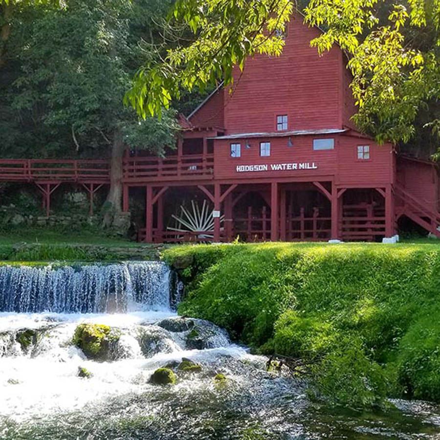Red watermill beside a small waterfall and lush green riverbank