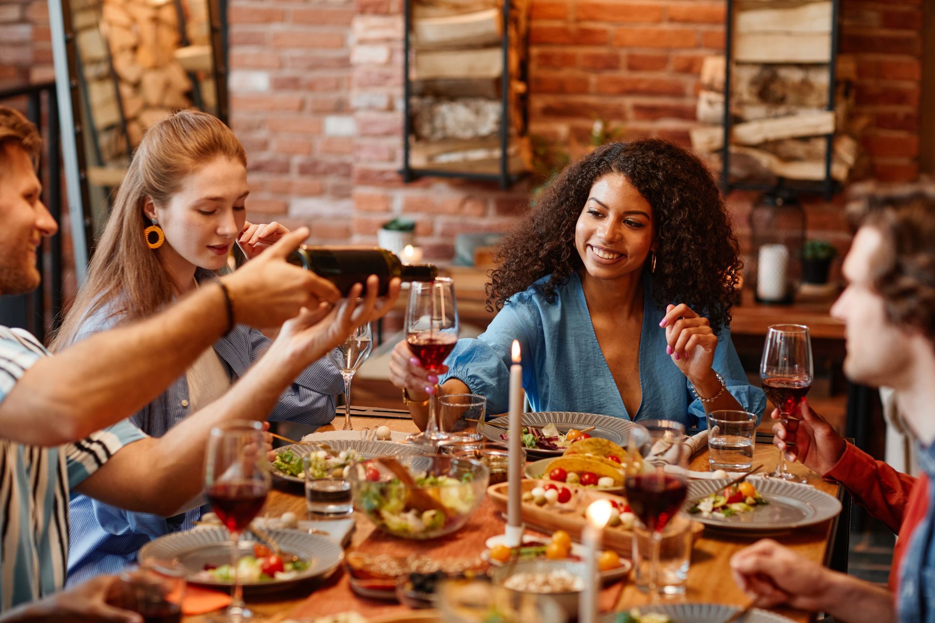 Friends sharing a meal and drinks at a rustic restaurant table with candles and red wine.