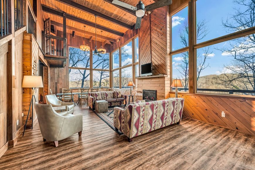 Rustic cabin living room with wood beams, large windows, and mountain views through the glass
