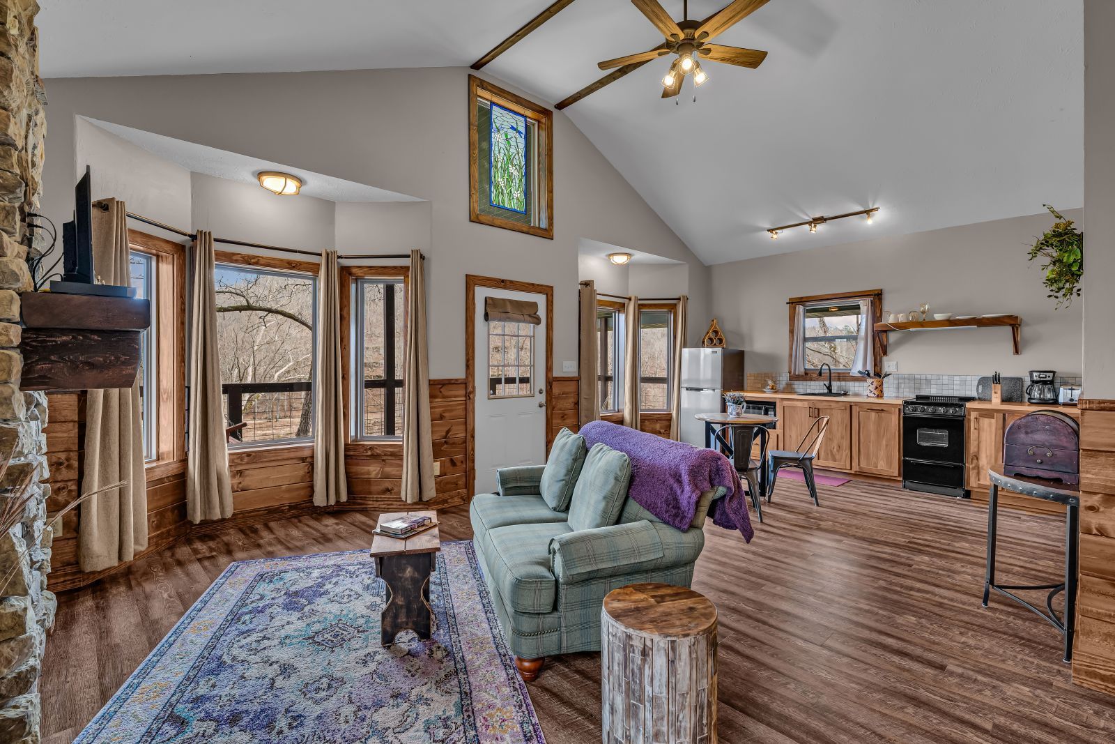 Open-concept living room with vaulted ceiling, teal chair, purple rug, and wood floors, leading to a dining area.