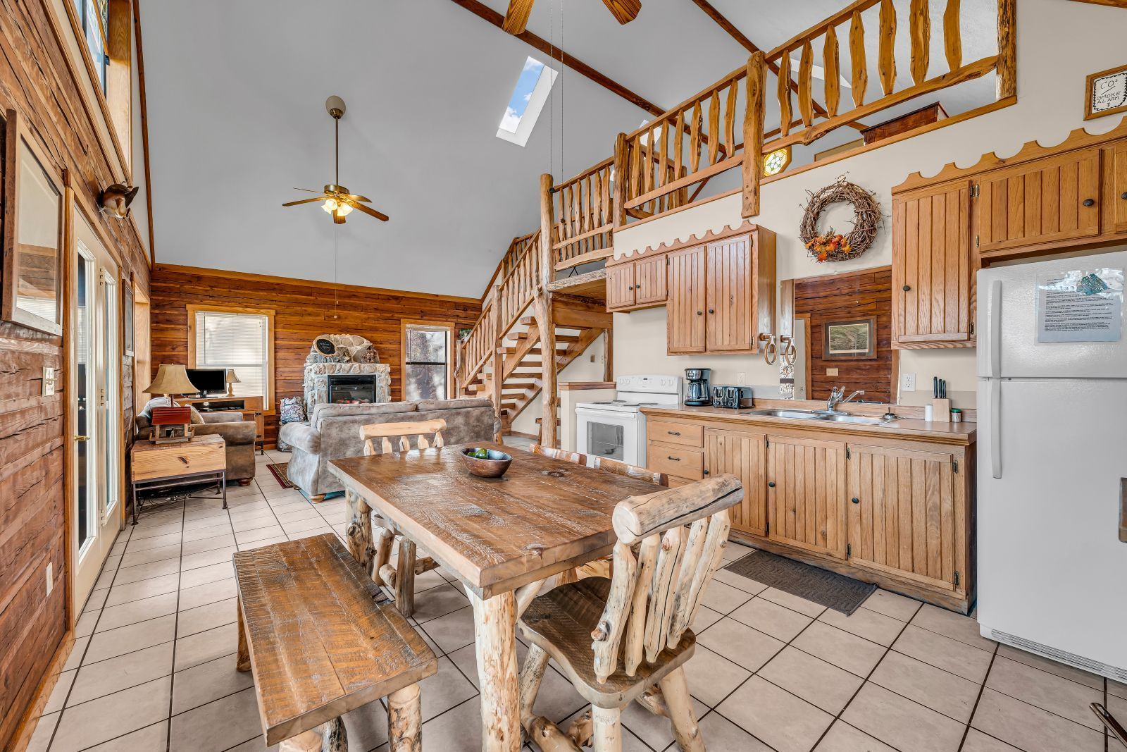 Rustic kitchen with wooden cabinets, central island, staircase, tiled floor, and white refrigerator