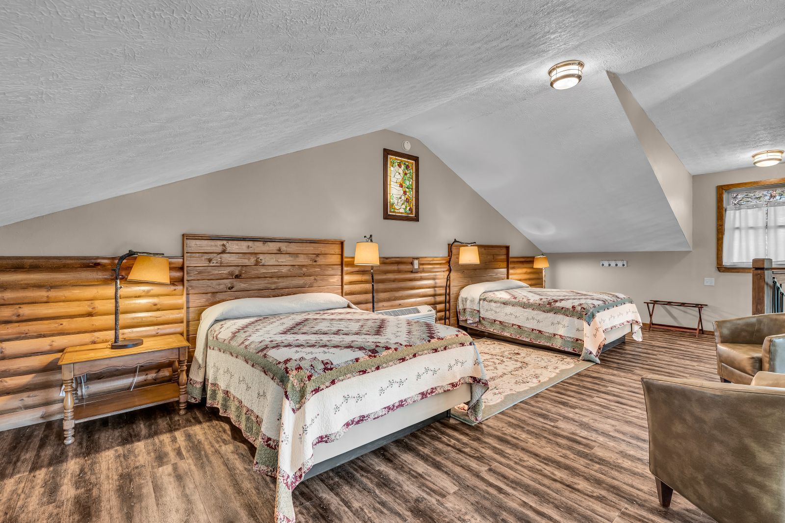 Cozy attic bedroom with two beds, wood-paneled walls, sloped ceiling, and patterned rugs