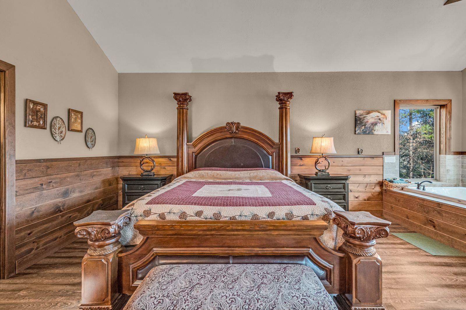 Elegant bedroom with a carved wooden bed, two dressers, and a window seat in warm neutral tones
