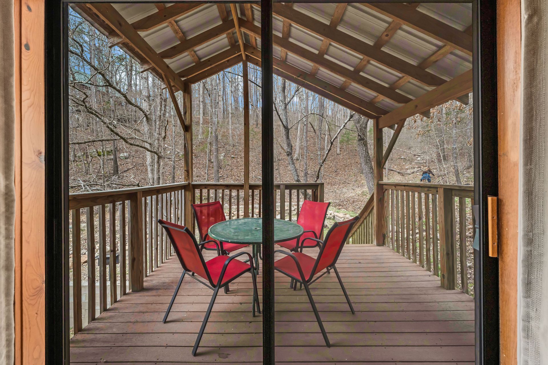 Covered wooden deck with a glass table and four red chairs overlooking trees