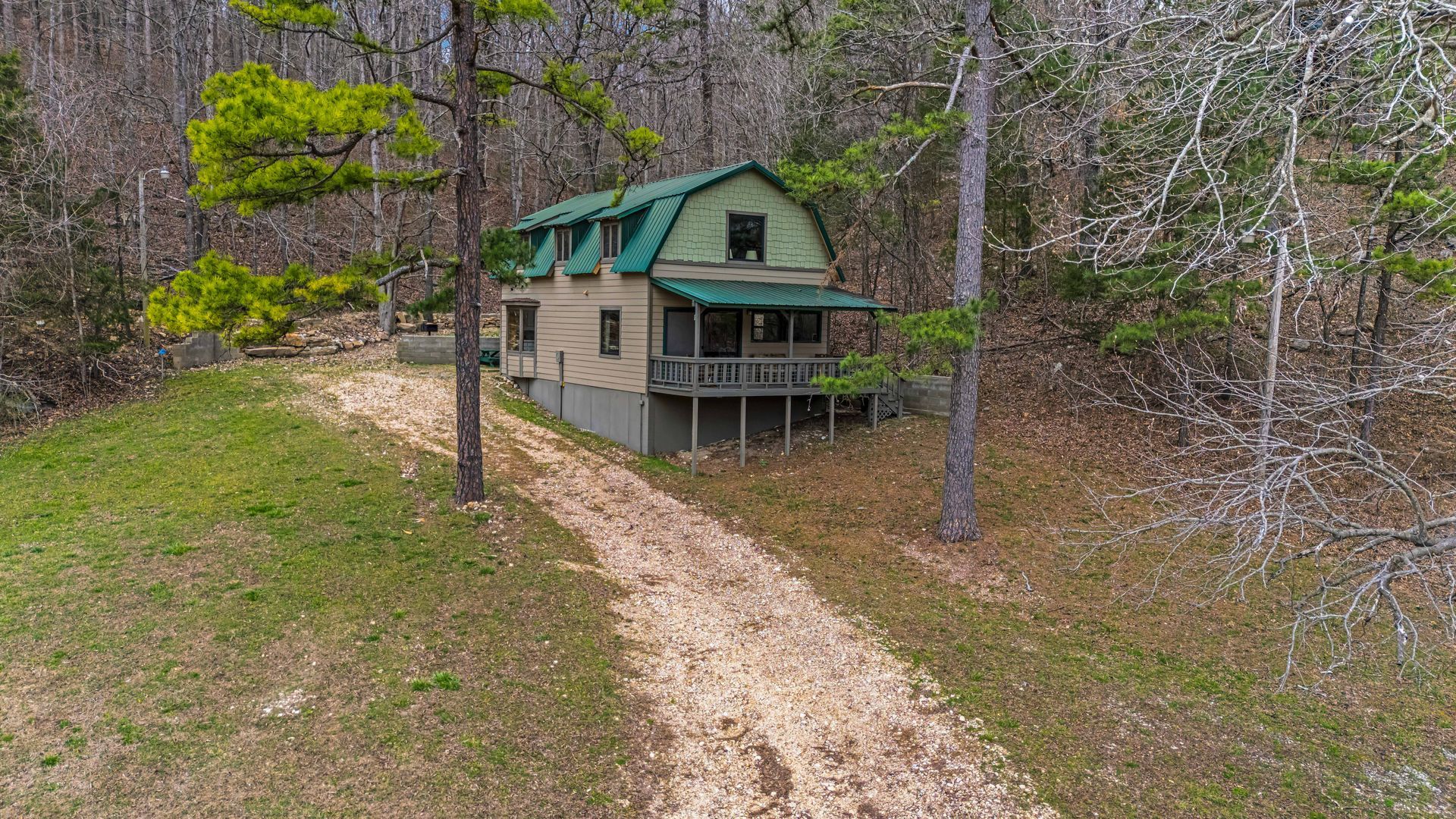 Small cabin with green roof on a wooded hillside beside a dirt road