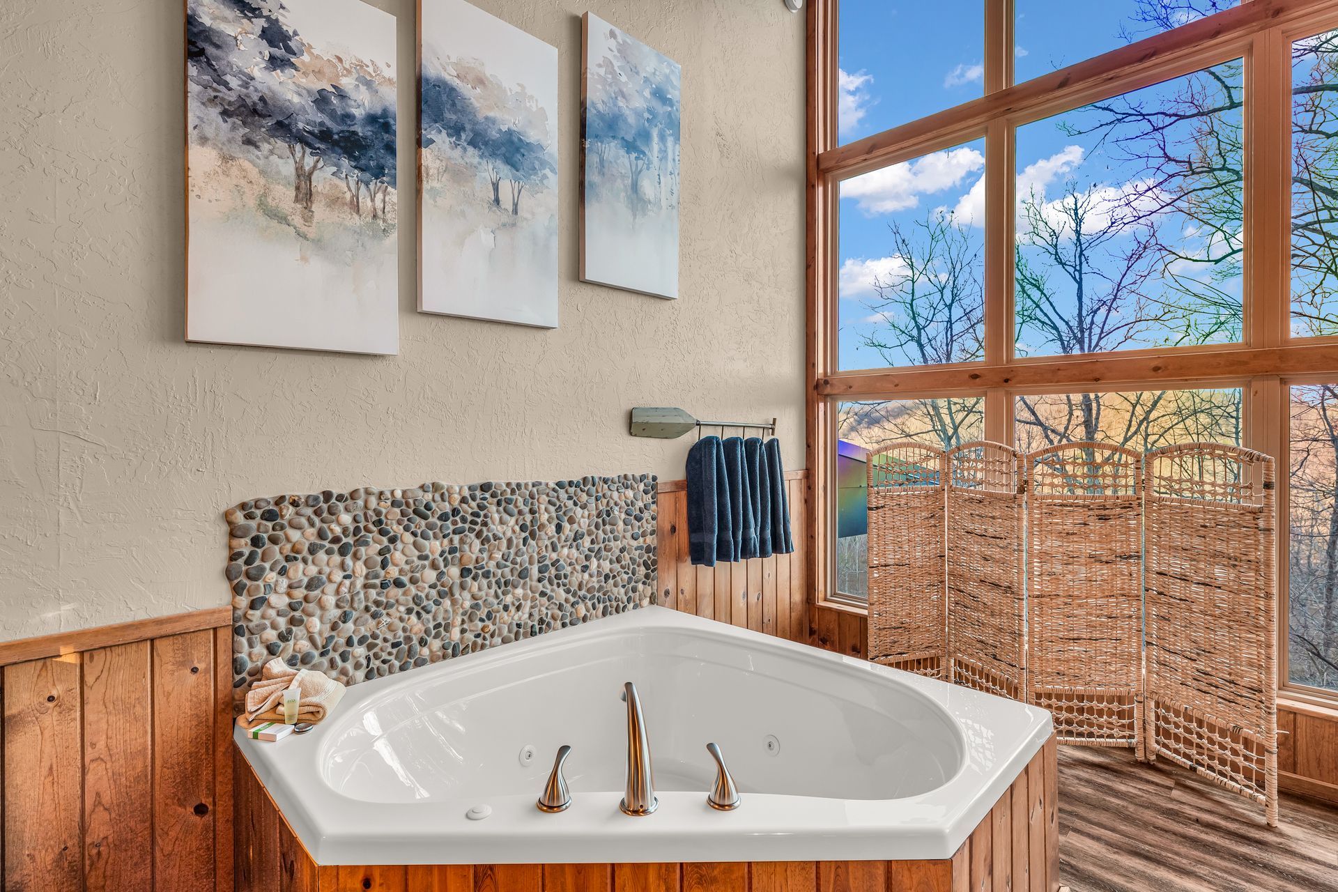 Modern bathroom with corner soaking tub, wood paneling, abstract wall art, and a large window.