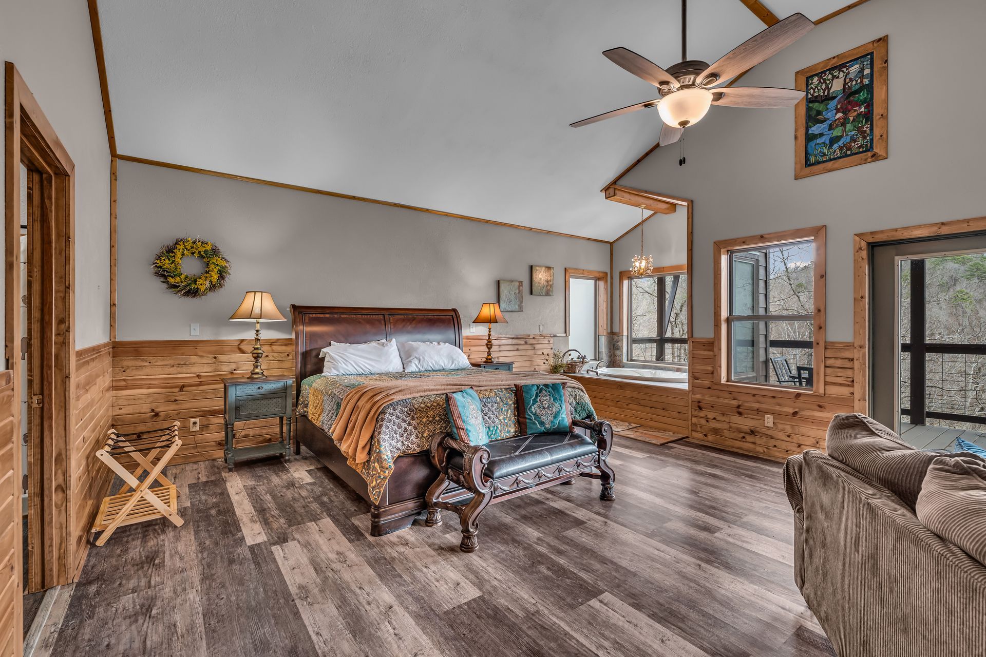 Cozy bedroom with a king bed, wood-paneled walls, ceiling fan, and patterned seating area
