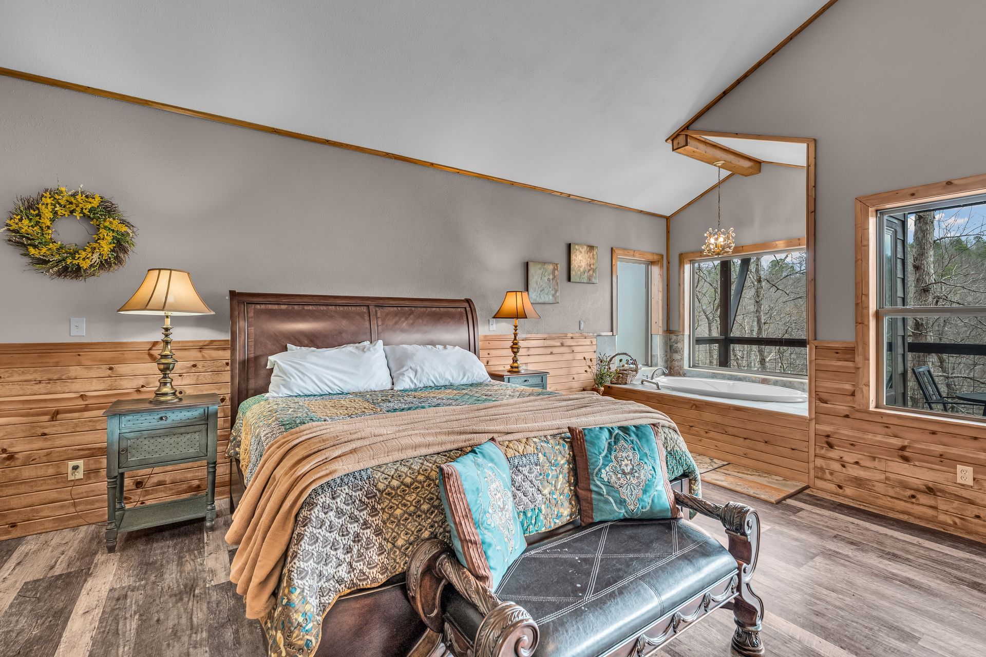 Bedroom with wood paneling, bed, lamps, and large windows overlooking trees.