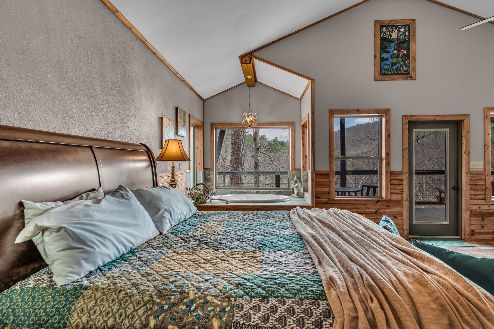 Cozy bedroom with a large bed, wood headboard, lamp, mirror, and vaulted ceiling with windows