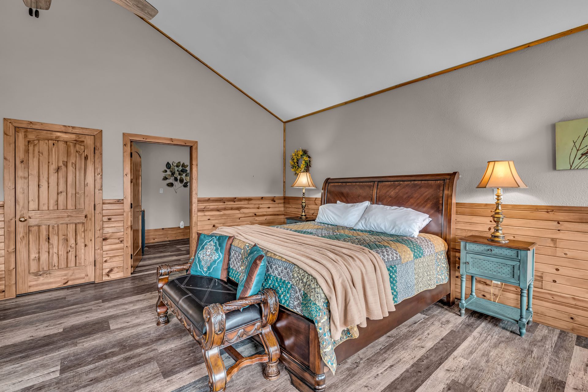 Cozy bedroom with wood-paneled accents, queen bed, teal nightstands, and soft lamp lighting