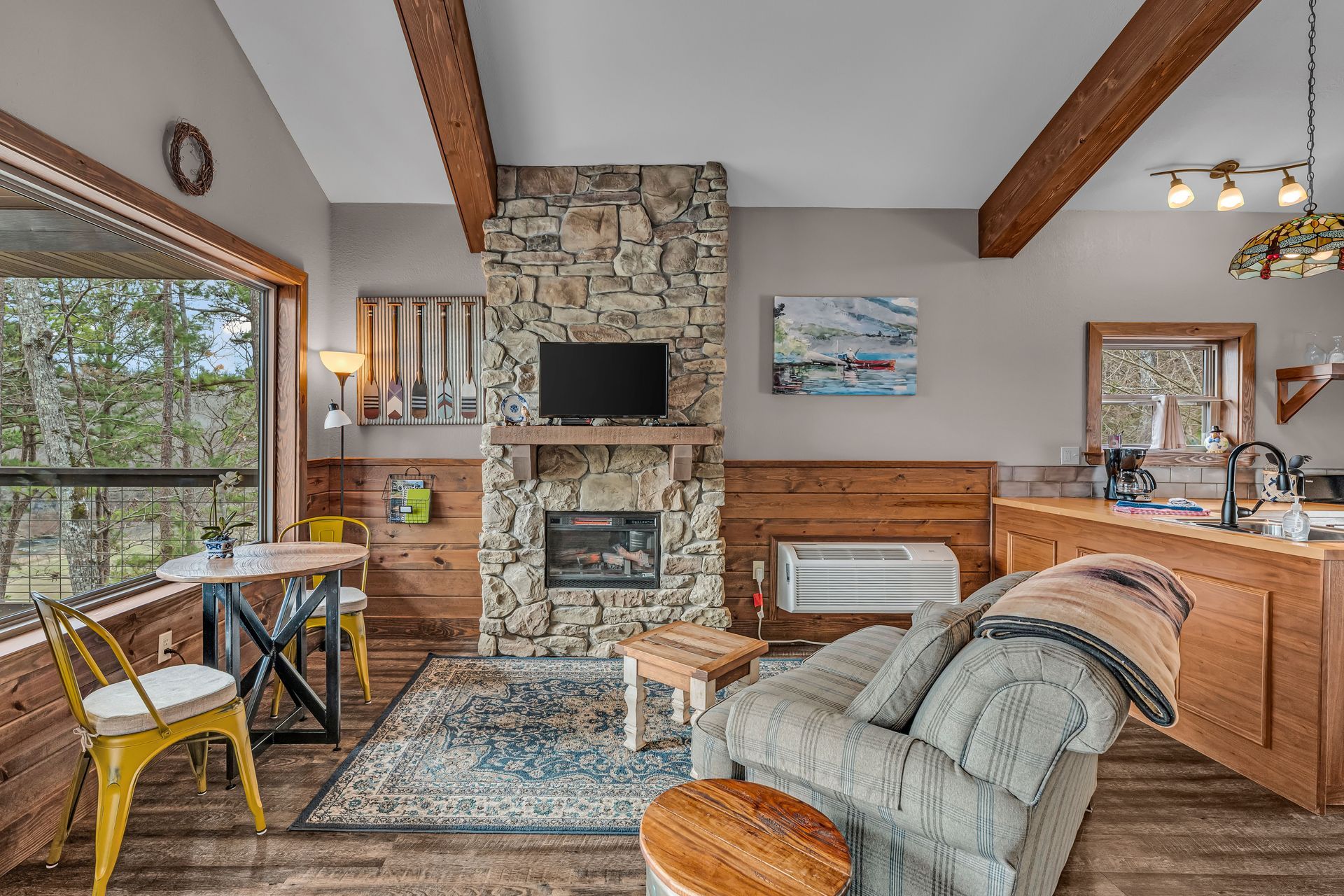 Cozy living room with stone fireplace, wood beams, leather chair, and large windows
