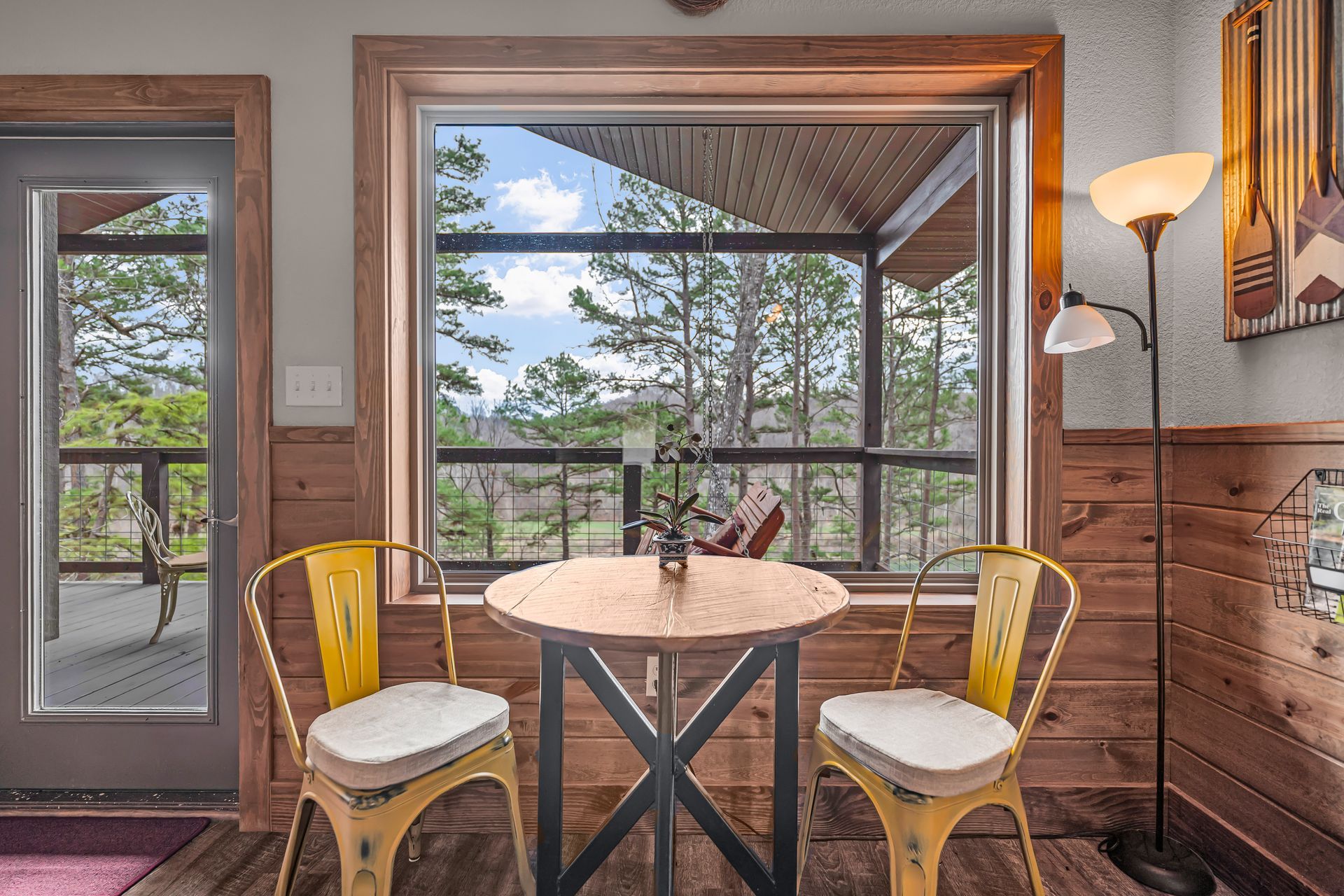Cozy sunroom with a round table, two chairs, and a large window view of trees and sky