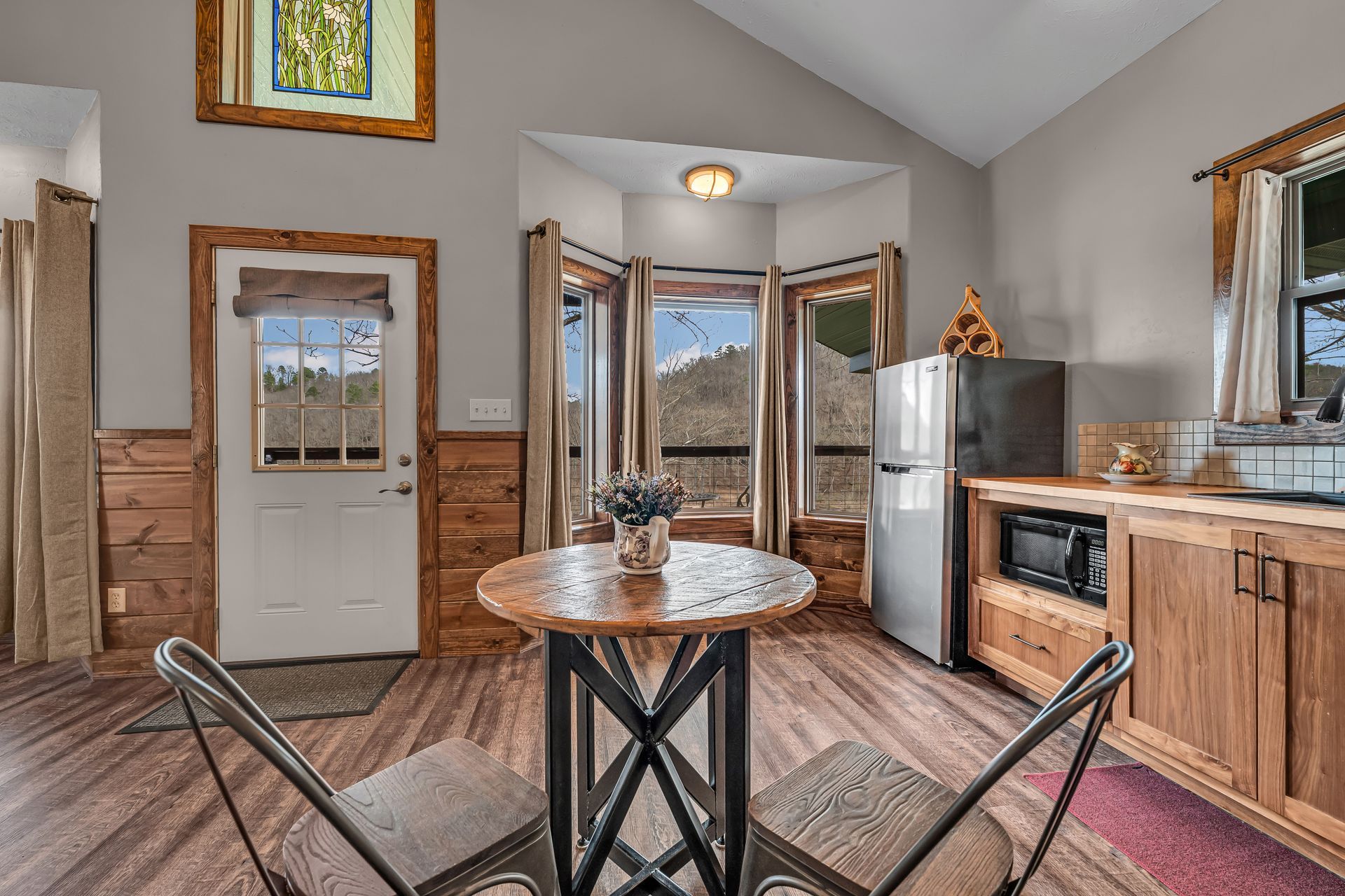 Small kitchen nook with round table, chairs, wood cabinets, and large windows overlooking mountains.