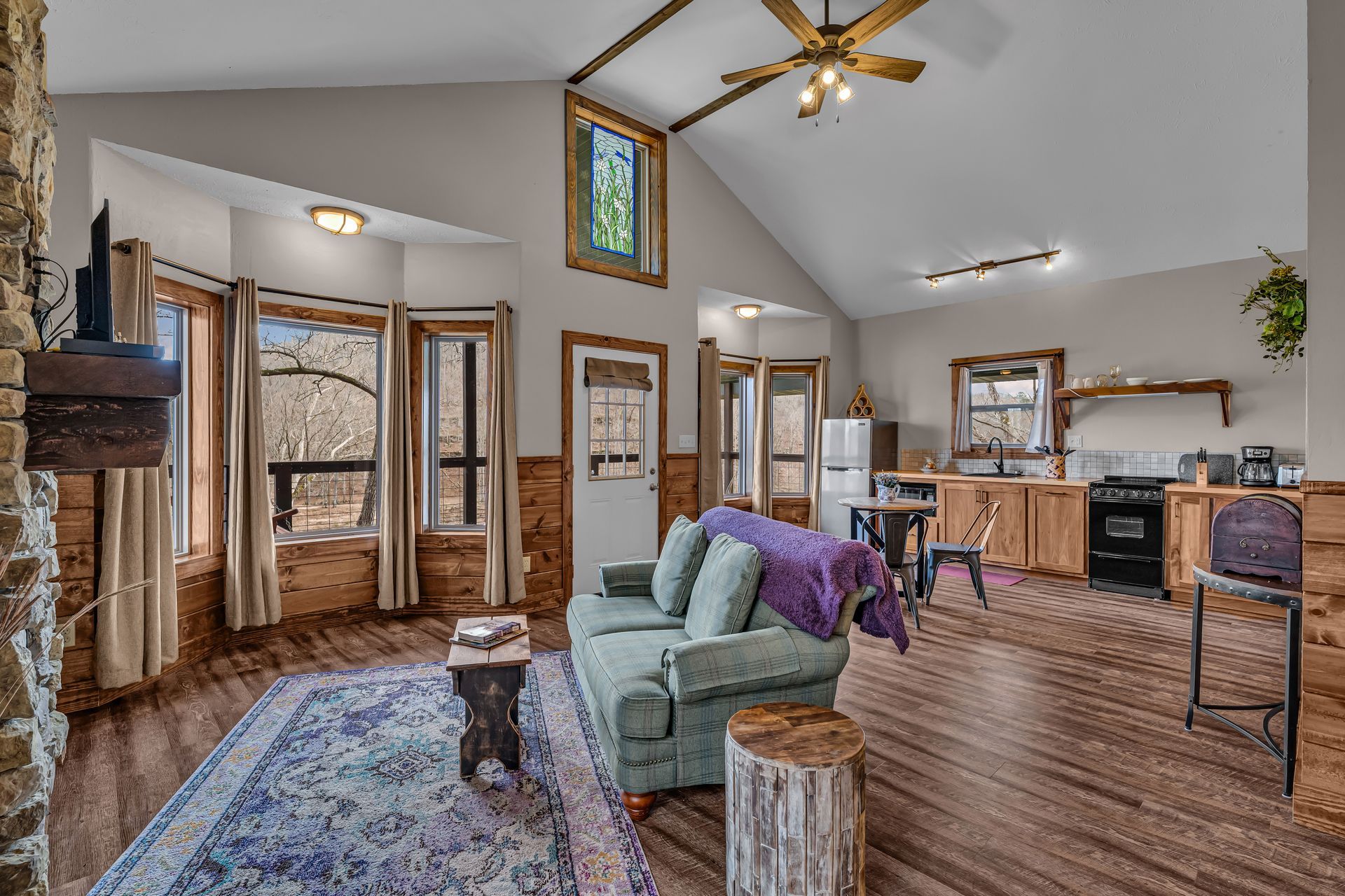 Open-concept living room with wood floors, teal chair, purple accents, and kitchen area in back