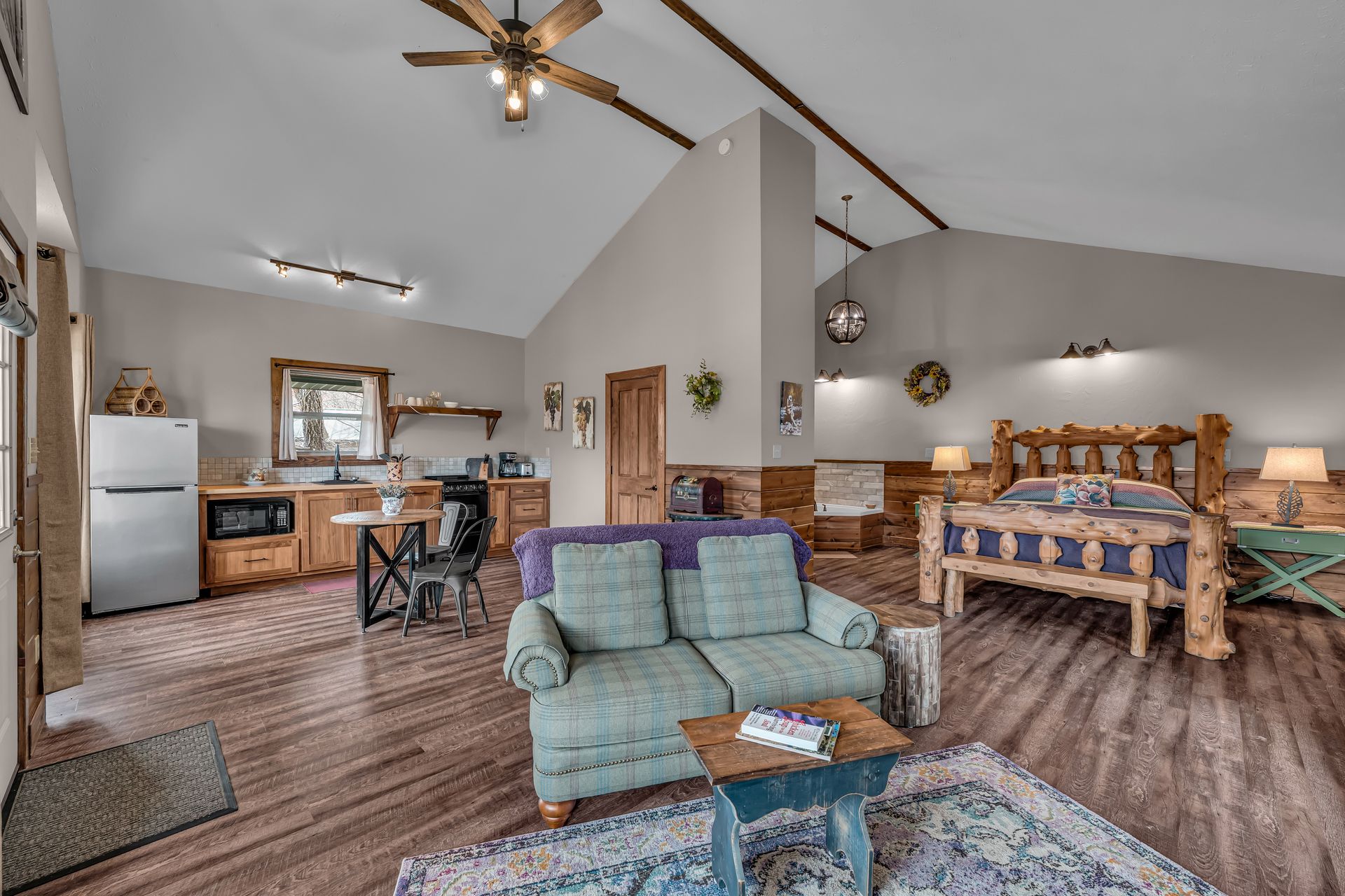 Open-concept living room and kitchen with vaulted ceiling, blue sofa, wood furniture, and ceiling fan