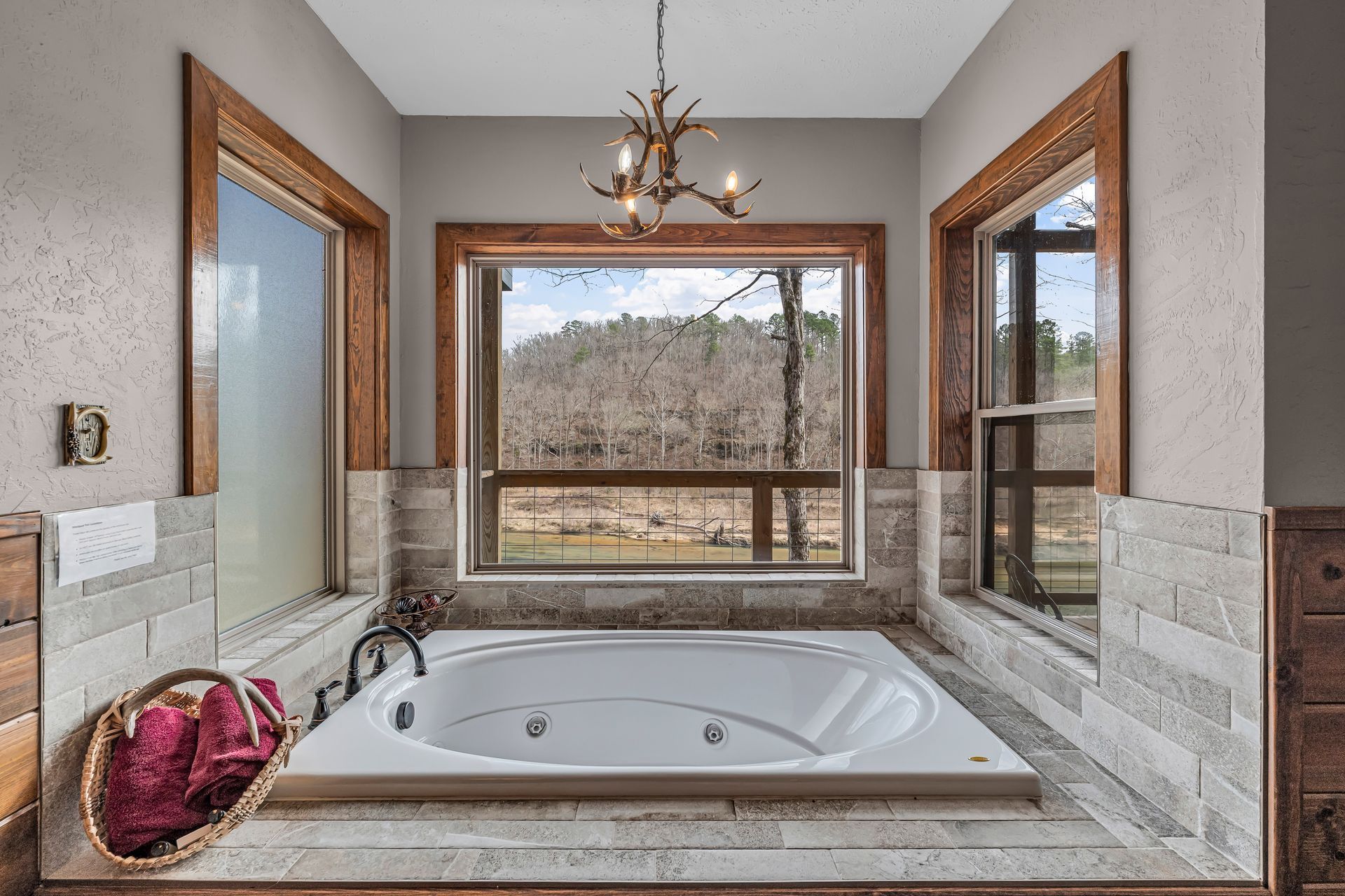 Spacious bathroom with a built-in soaking tub, large windows, and stone tile accents.