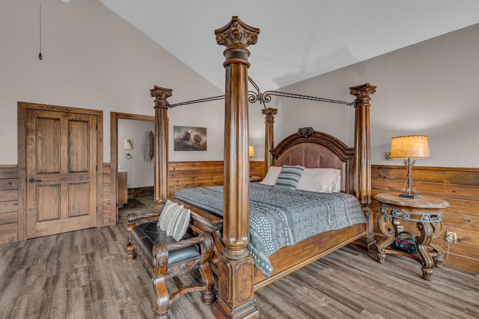 Ornate four-poster bed in a spacious bedroom with wood furniture and warm lamp lighting