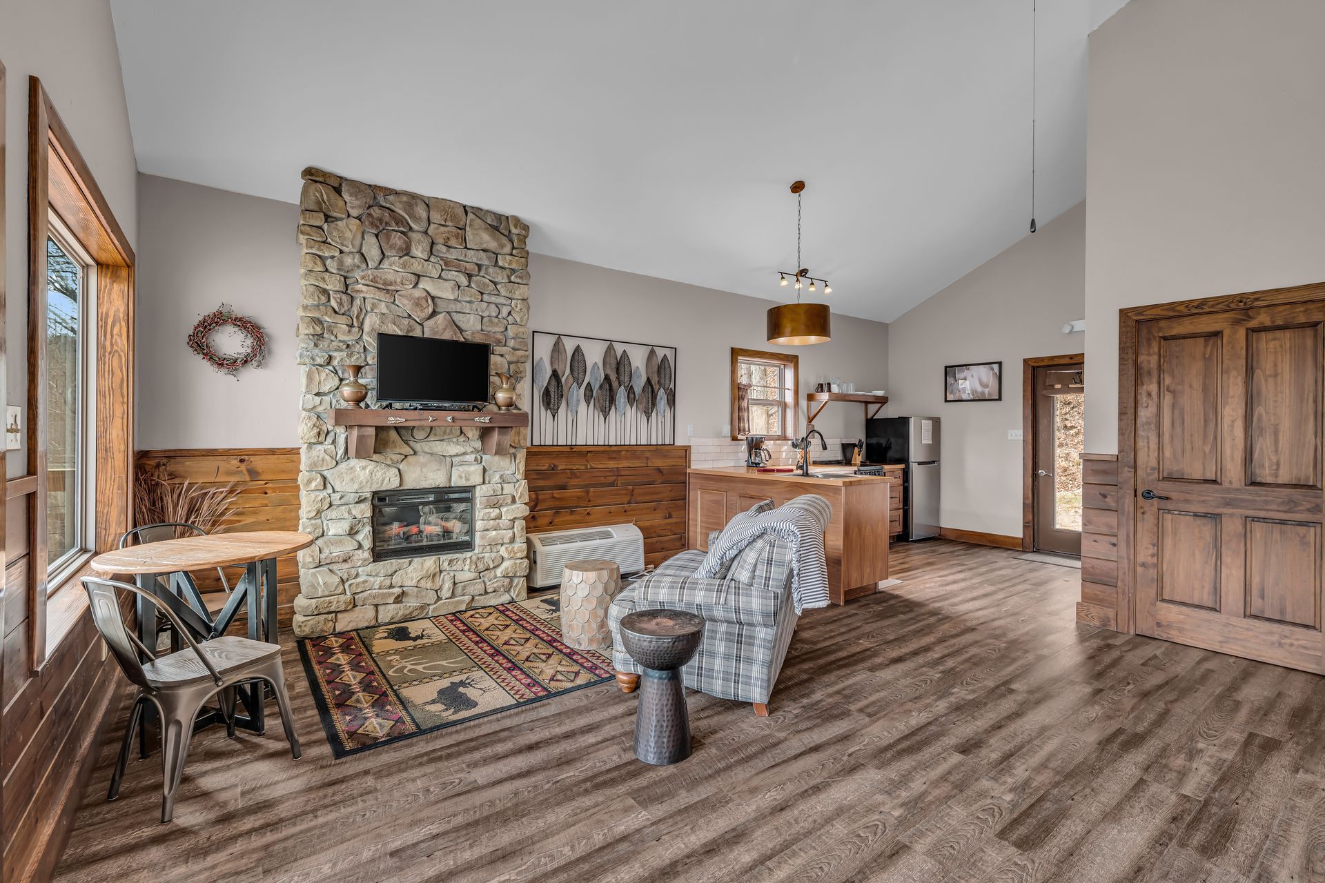 Open-concept living room with stone fireplace, wood floors, and warm brown furniture