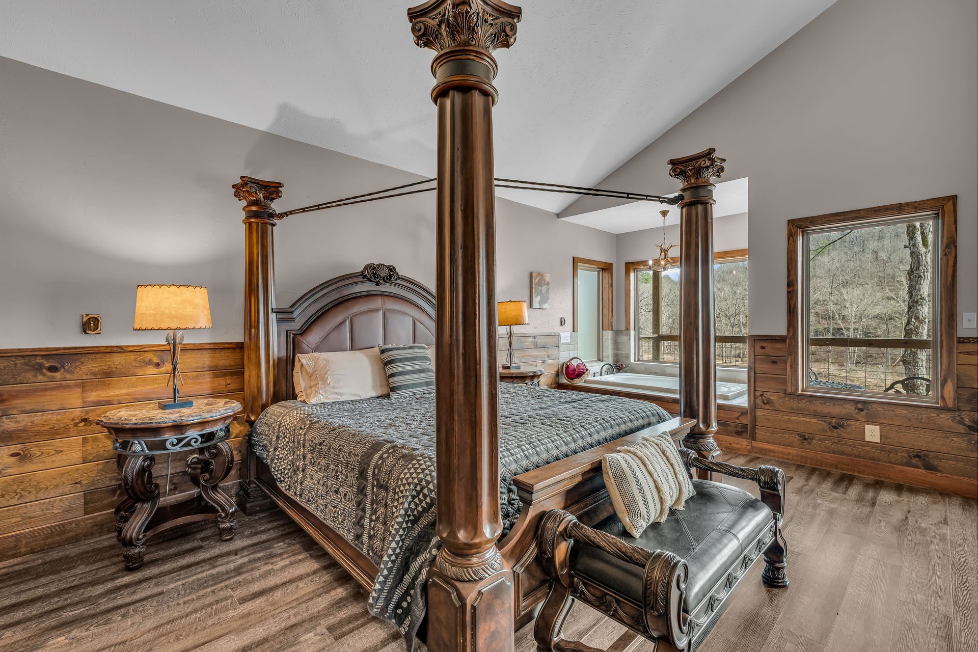 Rustic bedroom with four-poster bed, wood walls, and large windows overlooking trees