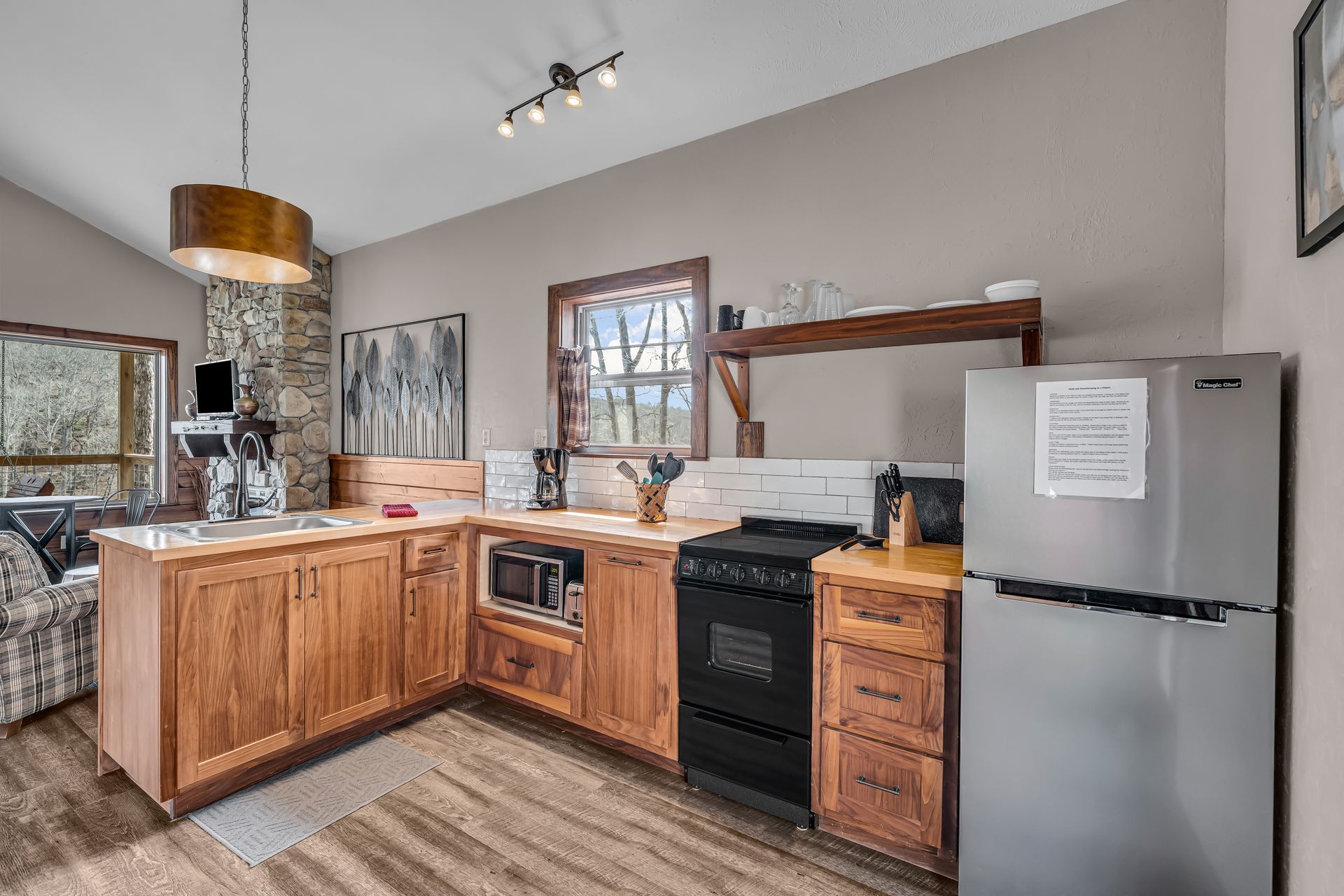 Small kitchen with wood cabinets, stainless fridge, black stove, and countertop under track lighting.