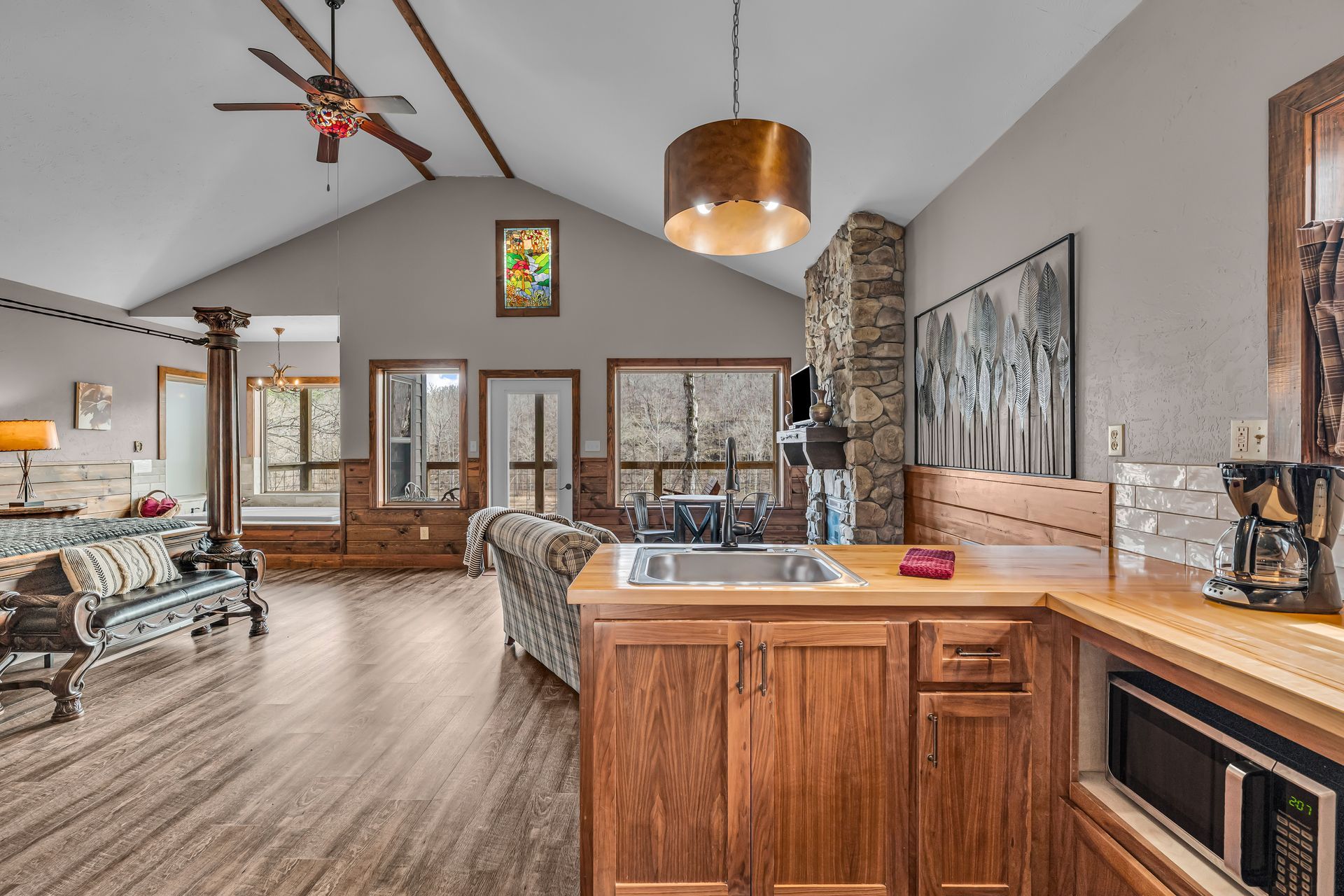 Open-concept living room and kitchen with wood floors, vaulted ceiling, stone fireplace, and large windows