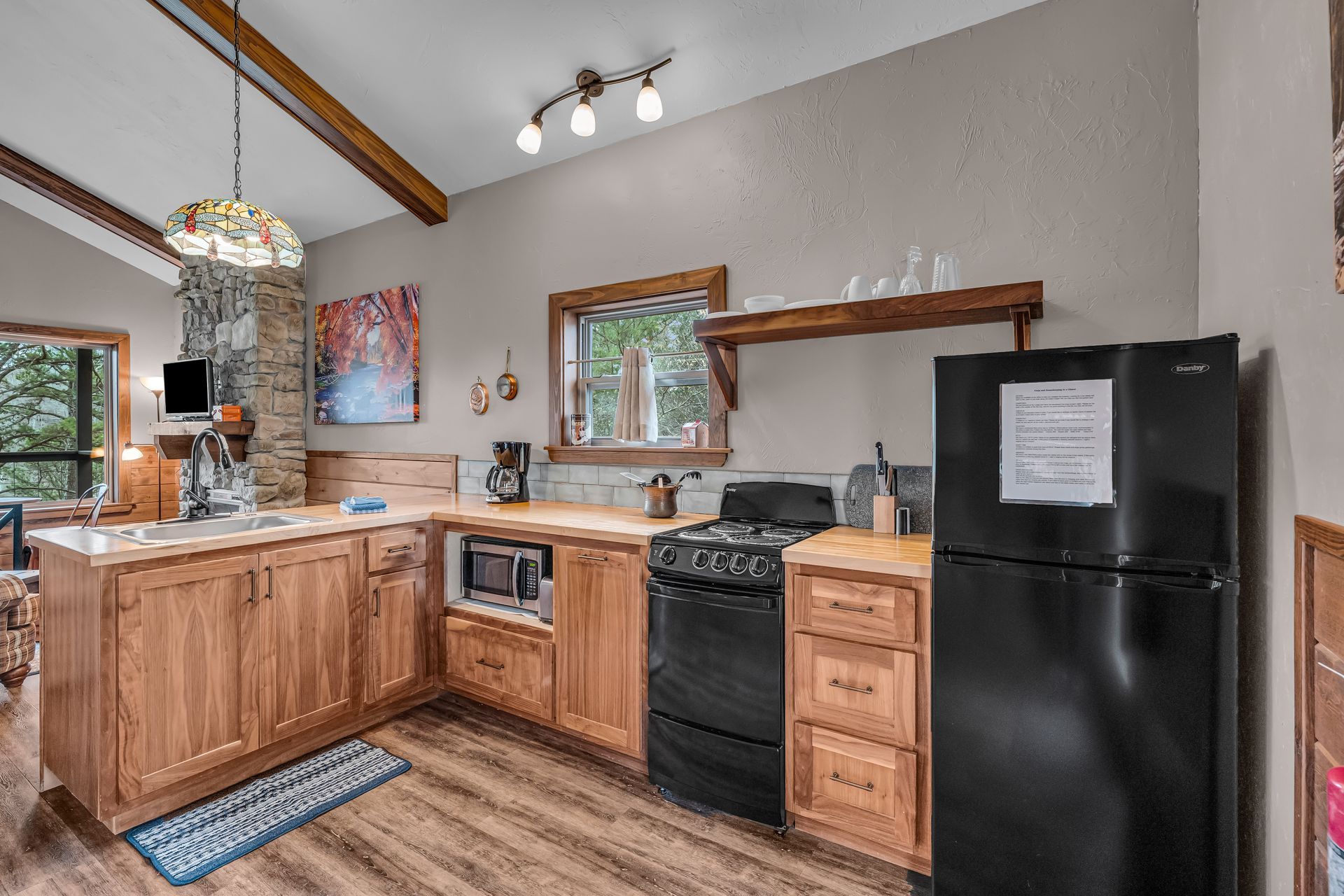 Rustic kitchen with wood cabinets, black appliances, and a tiled backsplash under vaulted ceiling.