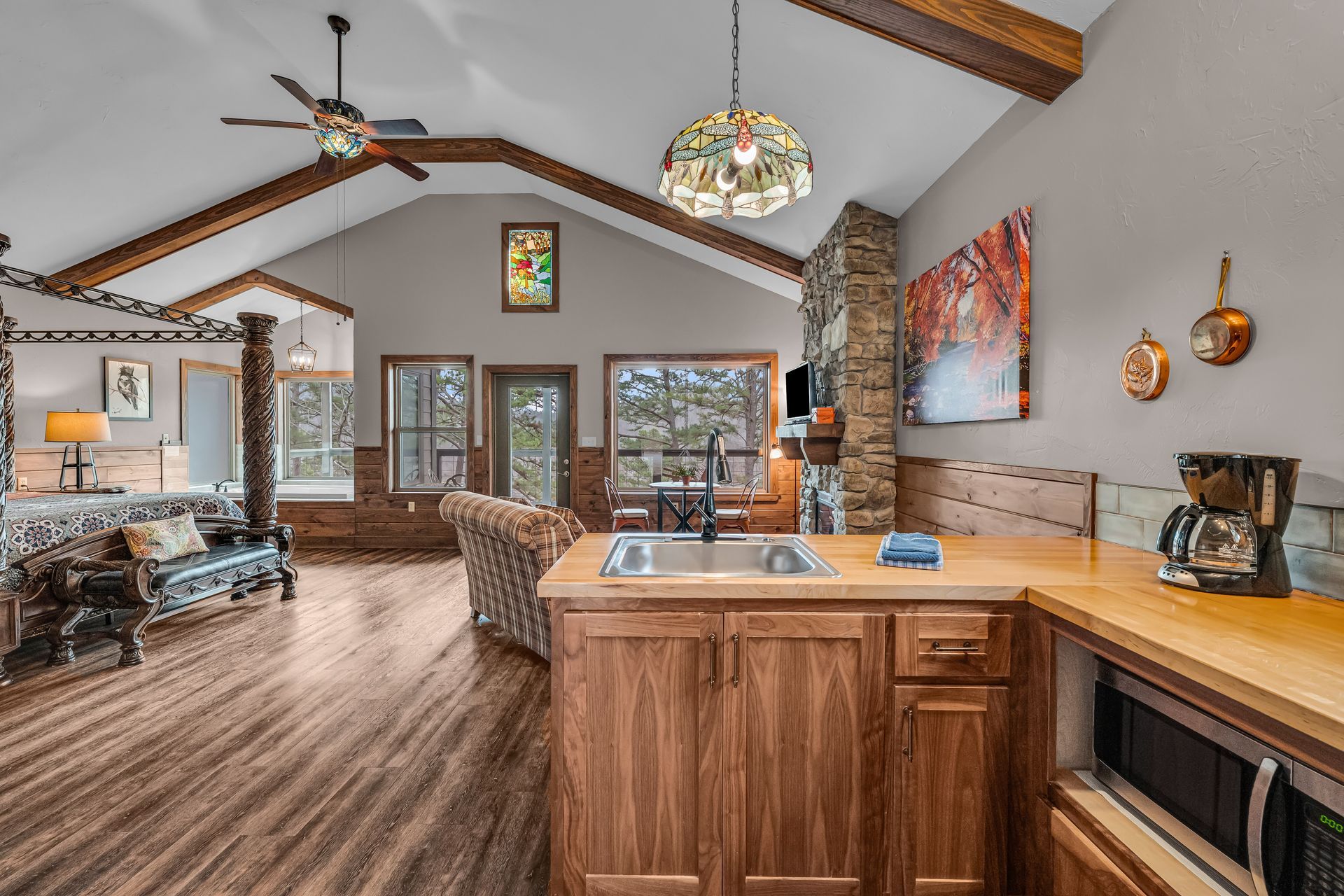 Open-concept living room and kitchen with vaulted wood ceilings, stone fireplace, and large windows.