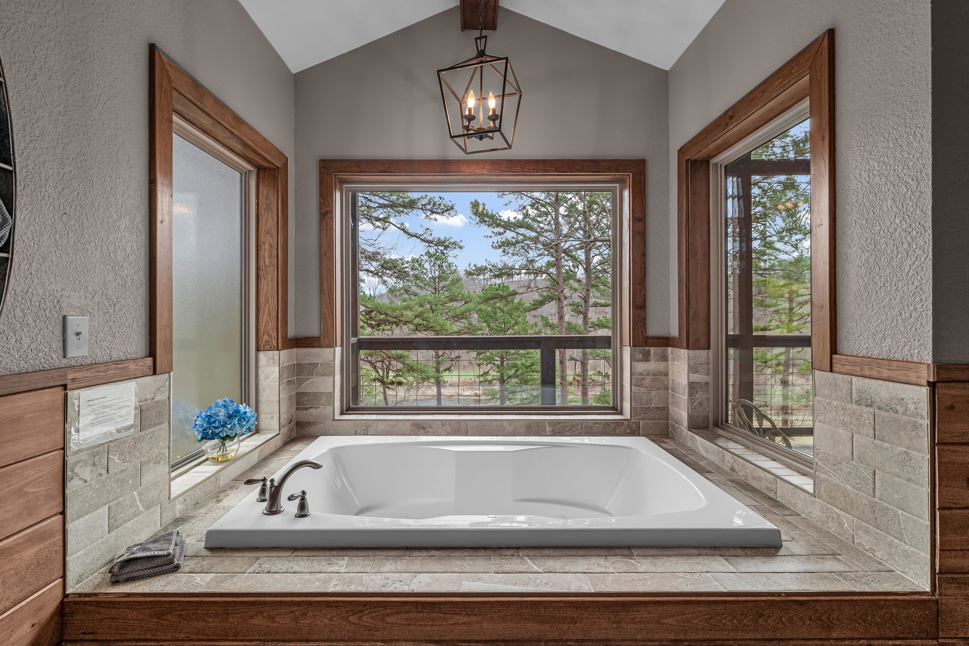 Modern bathroom with a soaking tub and large windows overlooking trees and a deck
