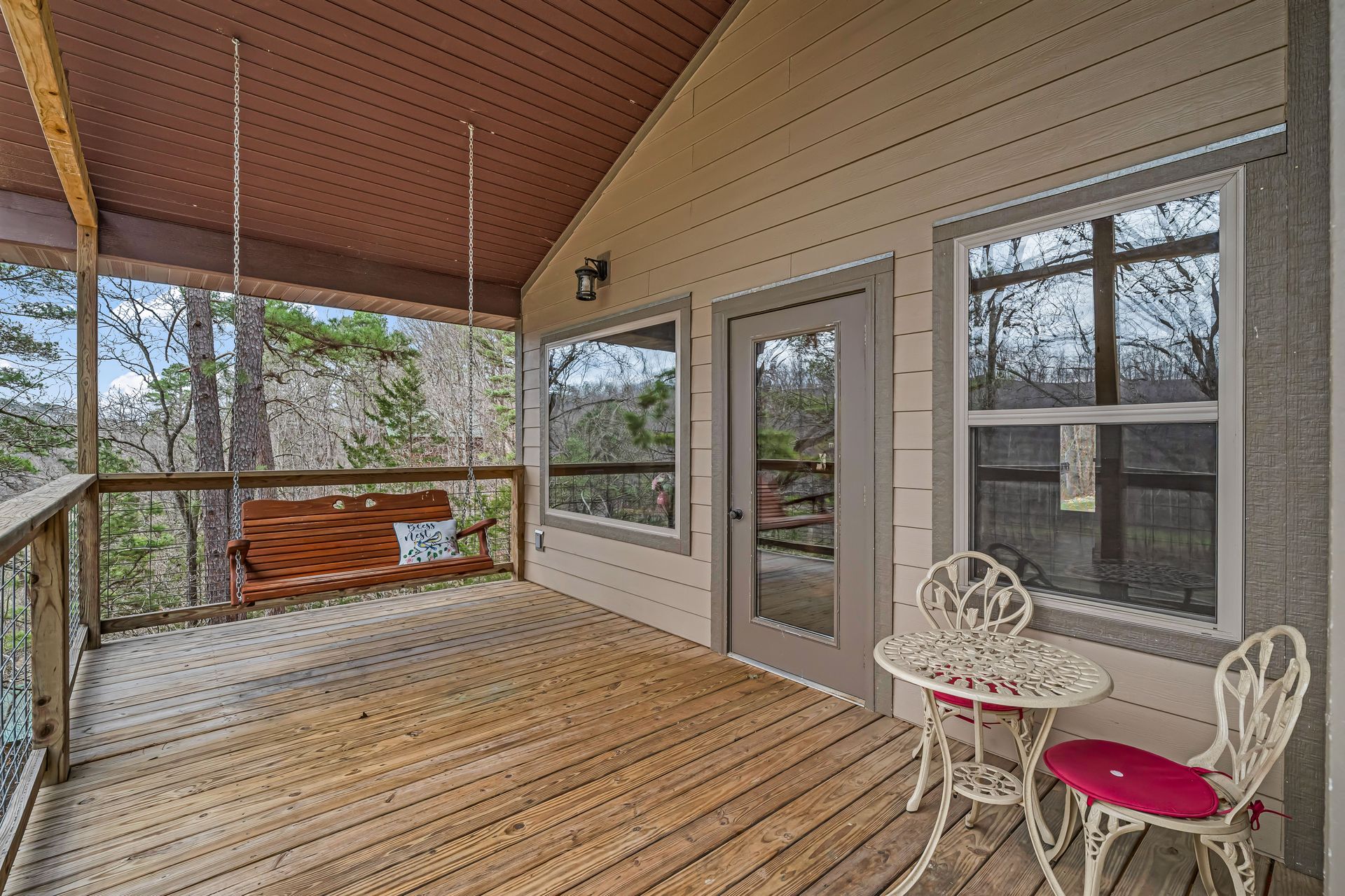 Covered wooden porch with screened windows, glass door, and a small white table and pink chair.