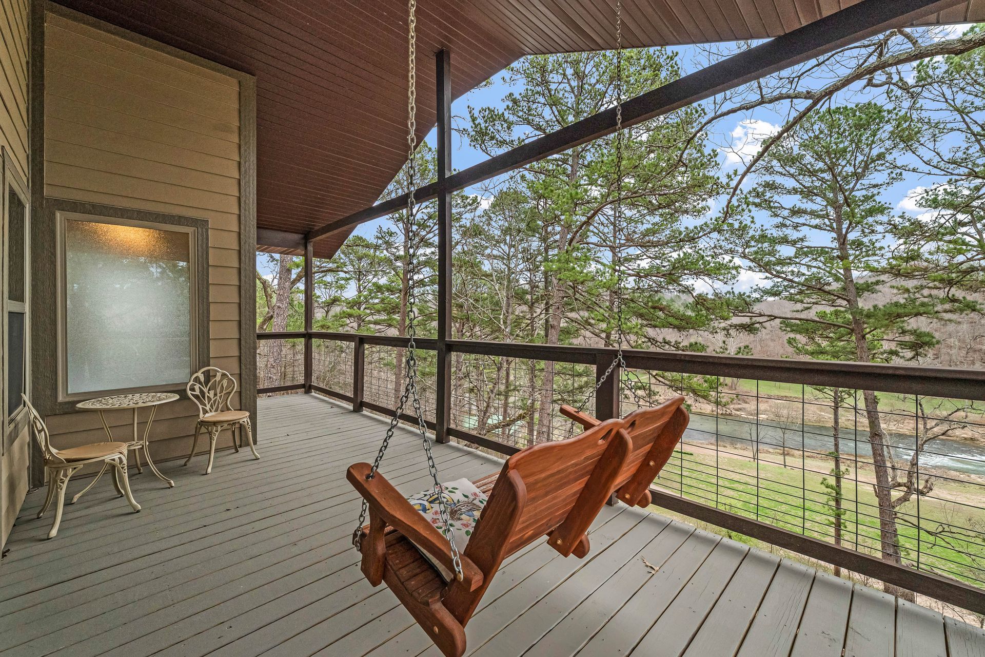 Covered porch with two wooden chairs and a screened view of trees and a yard