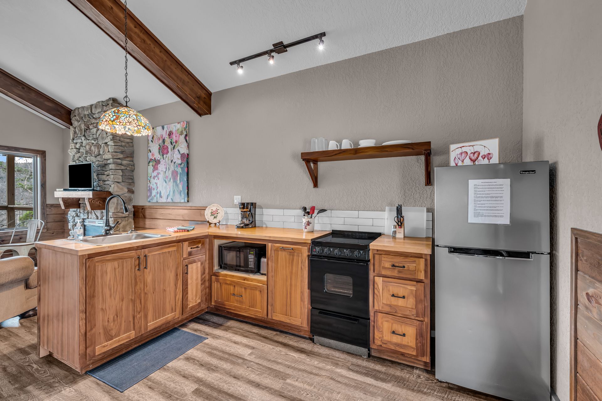 Rustic kitchen with wooden cabinets, stainless fridge, black stove, and open shelving