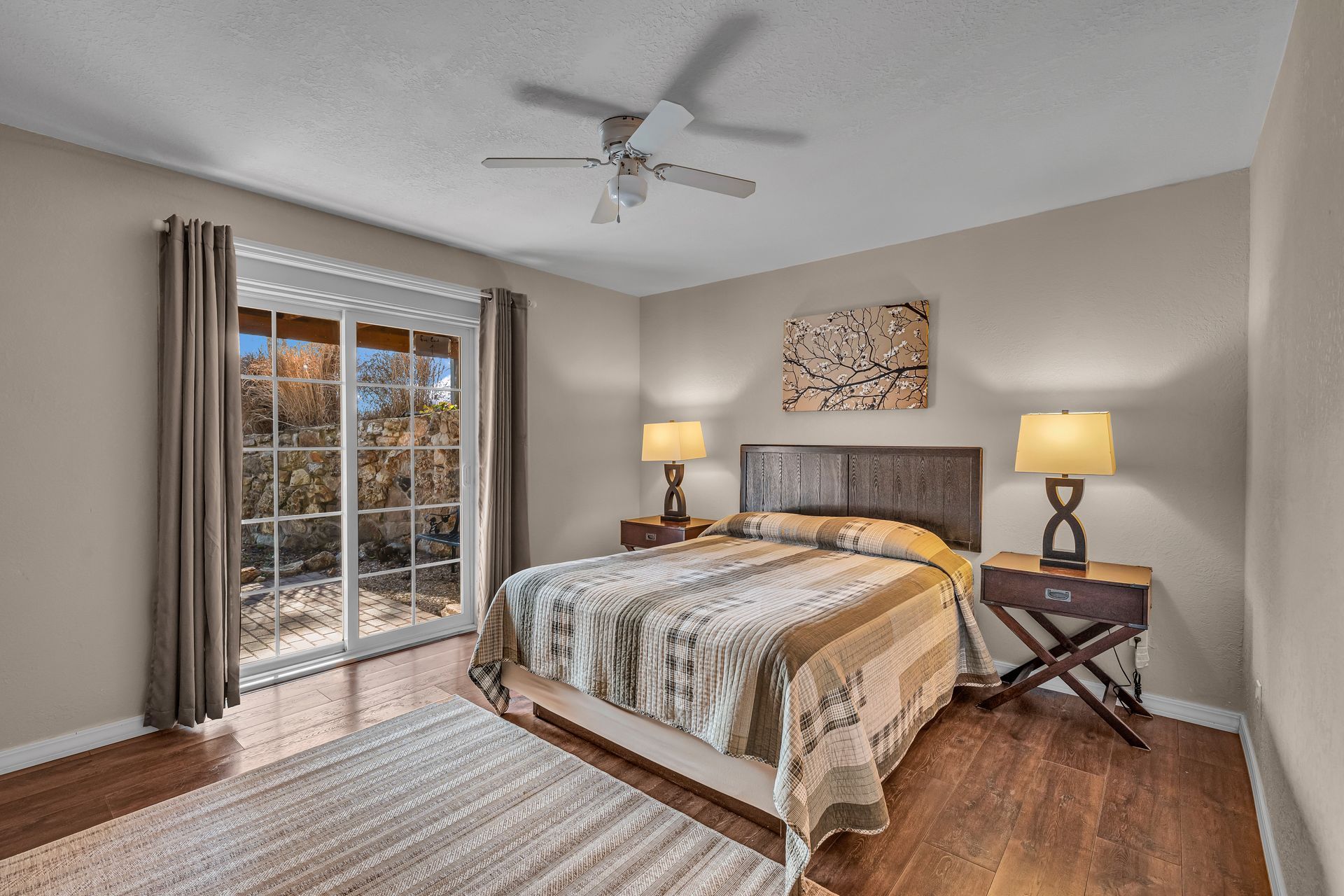 Bedroom with a bed, two lamps, sliding glass doors, and a ceiling fan