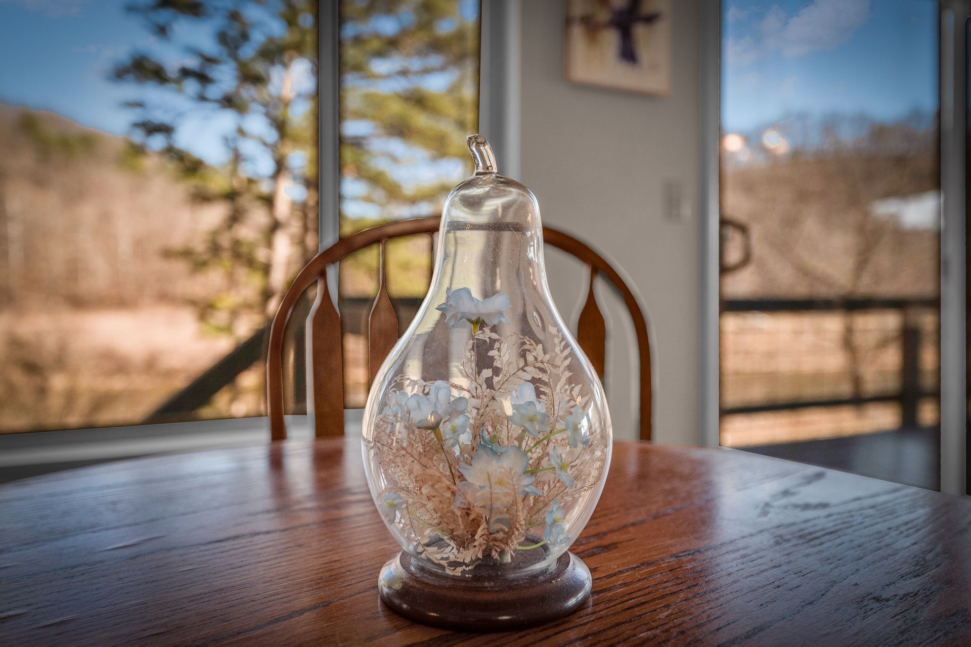 Clear glass decorative bottle on a wooden table by a sunny window with blurred trees outside