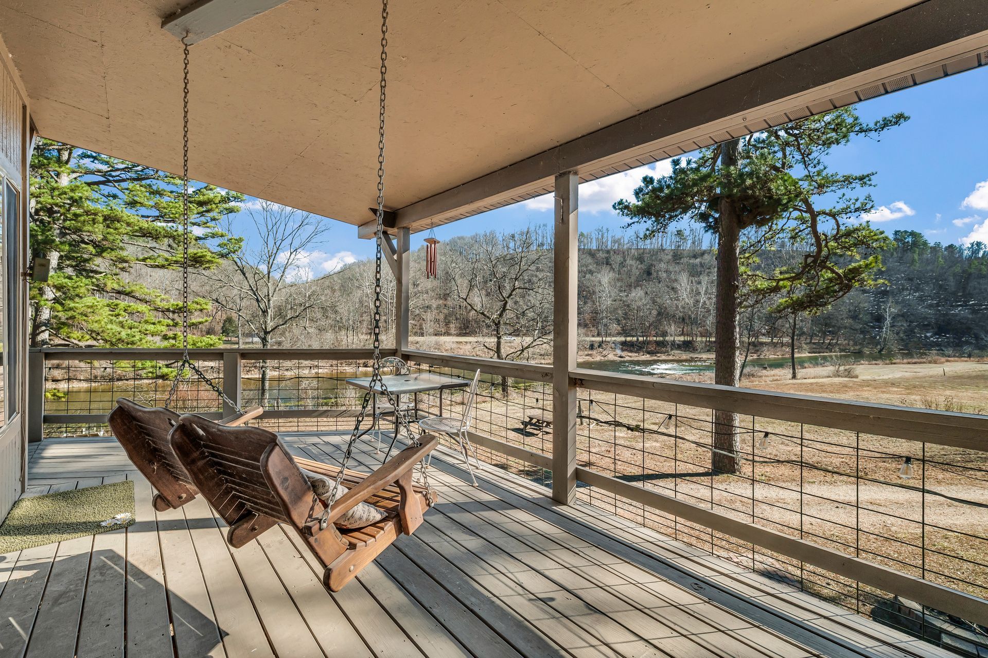 Covered porch with two lounge chairs, metal railing, and a view of trees and mountains beyond.