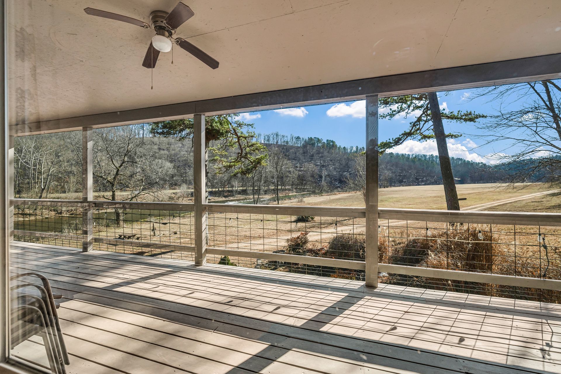Covered patio with ceiling fan and large windows overlooking a sunny yard and distant mountains