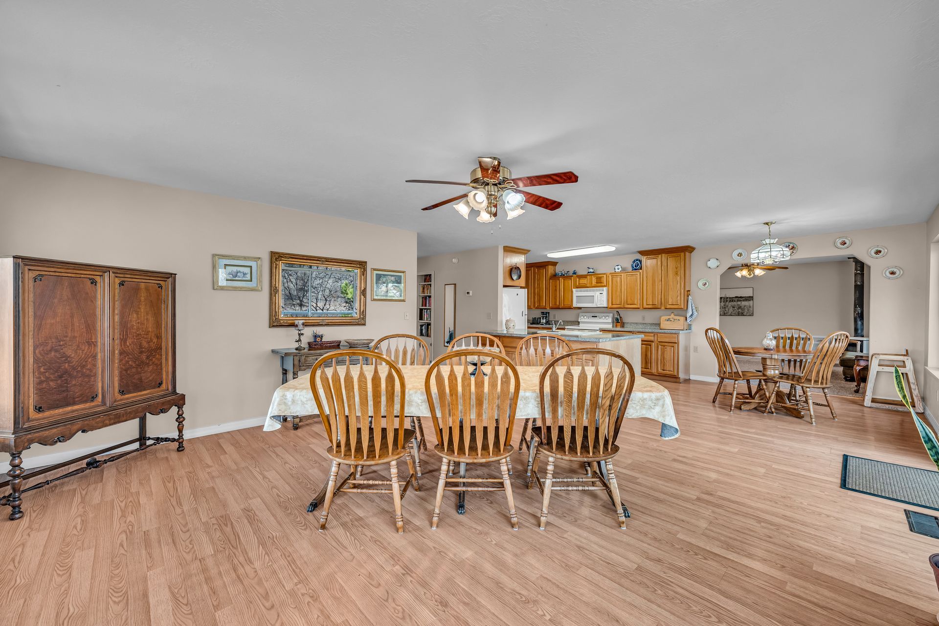 Open-concept dining and living room with wooden chairs, ceiling fan, and kitchen in the background