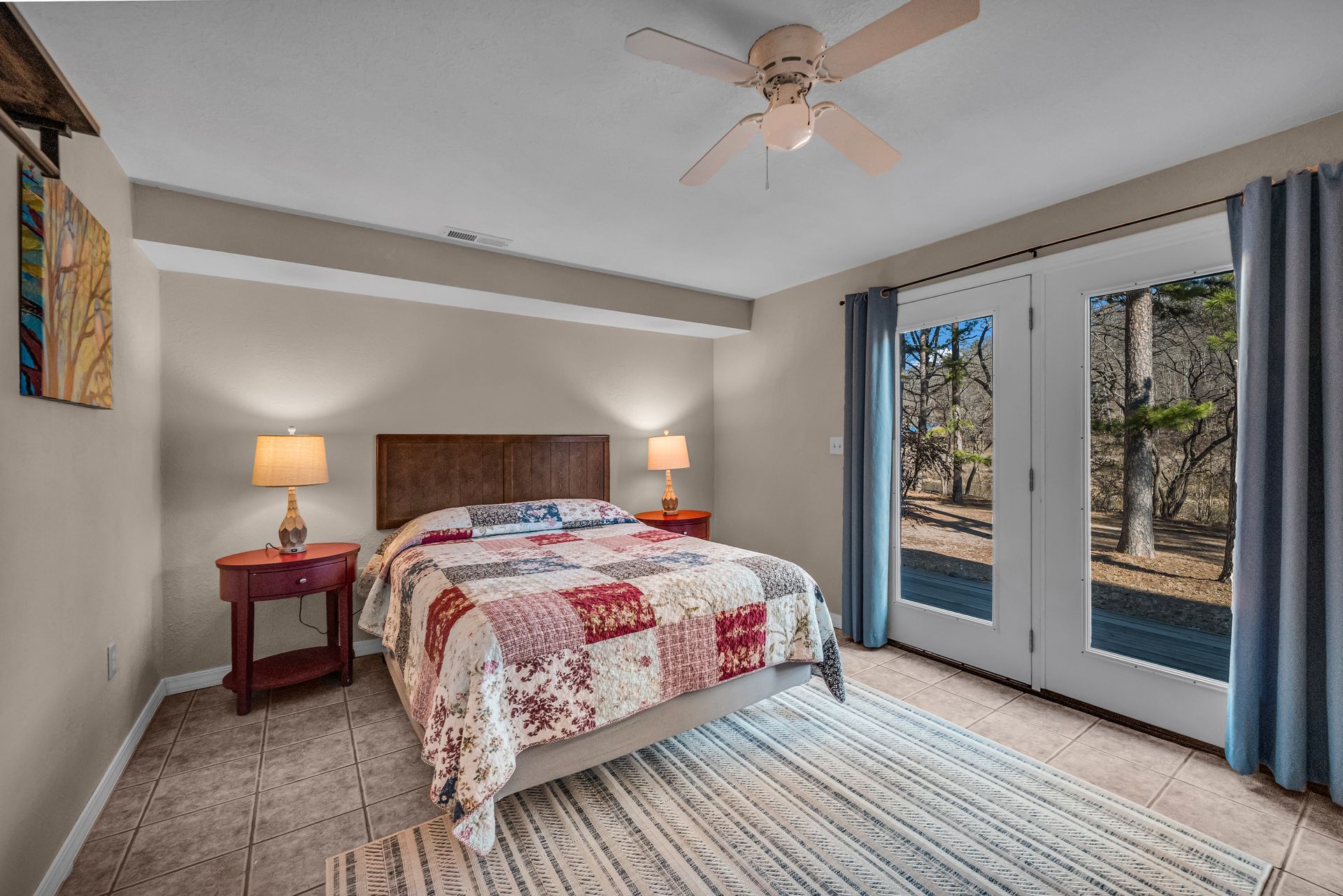 Bedroom with king bed, bedside lamps, ceiling fan, and sliding glass doors to a wooded view.
