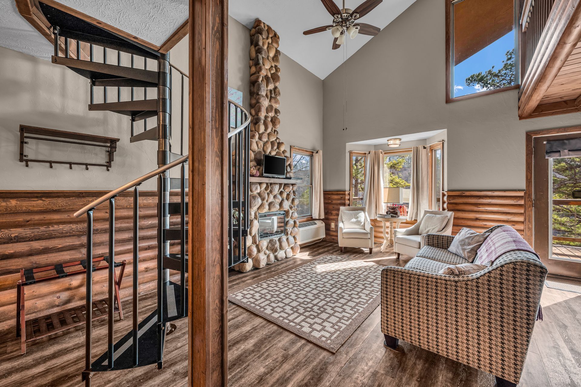Spacious loft living room with spiral staircase, brick fireplace, wicker sofa, and bright windows