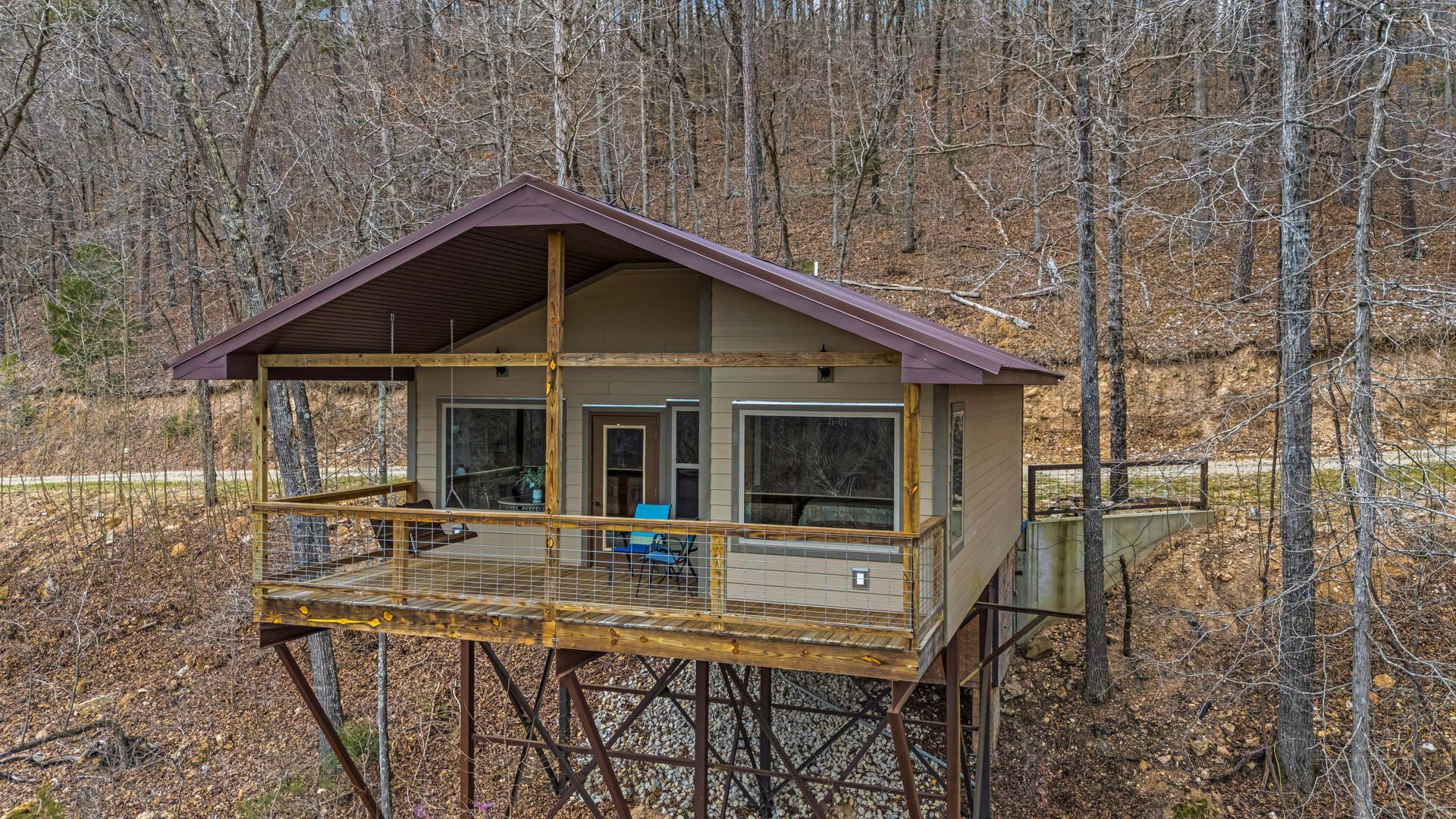 Small cabin on stilts with a porch in a wooded hillside setting