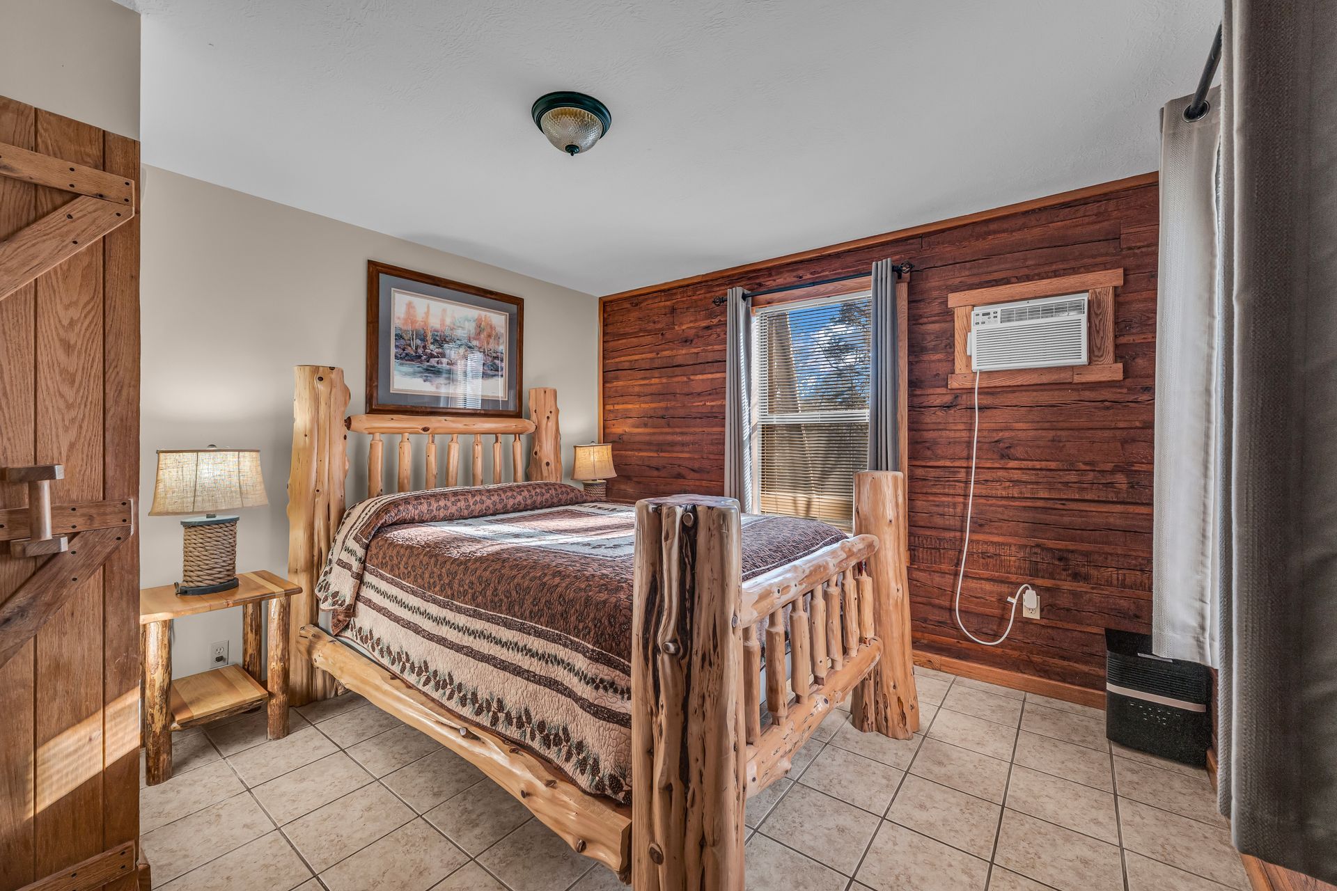 Cozy bedroom with log bed, brick accent wall, and tiled floor next to a windowed door