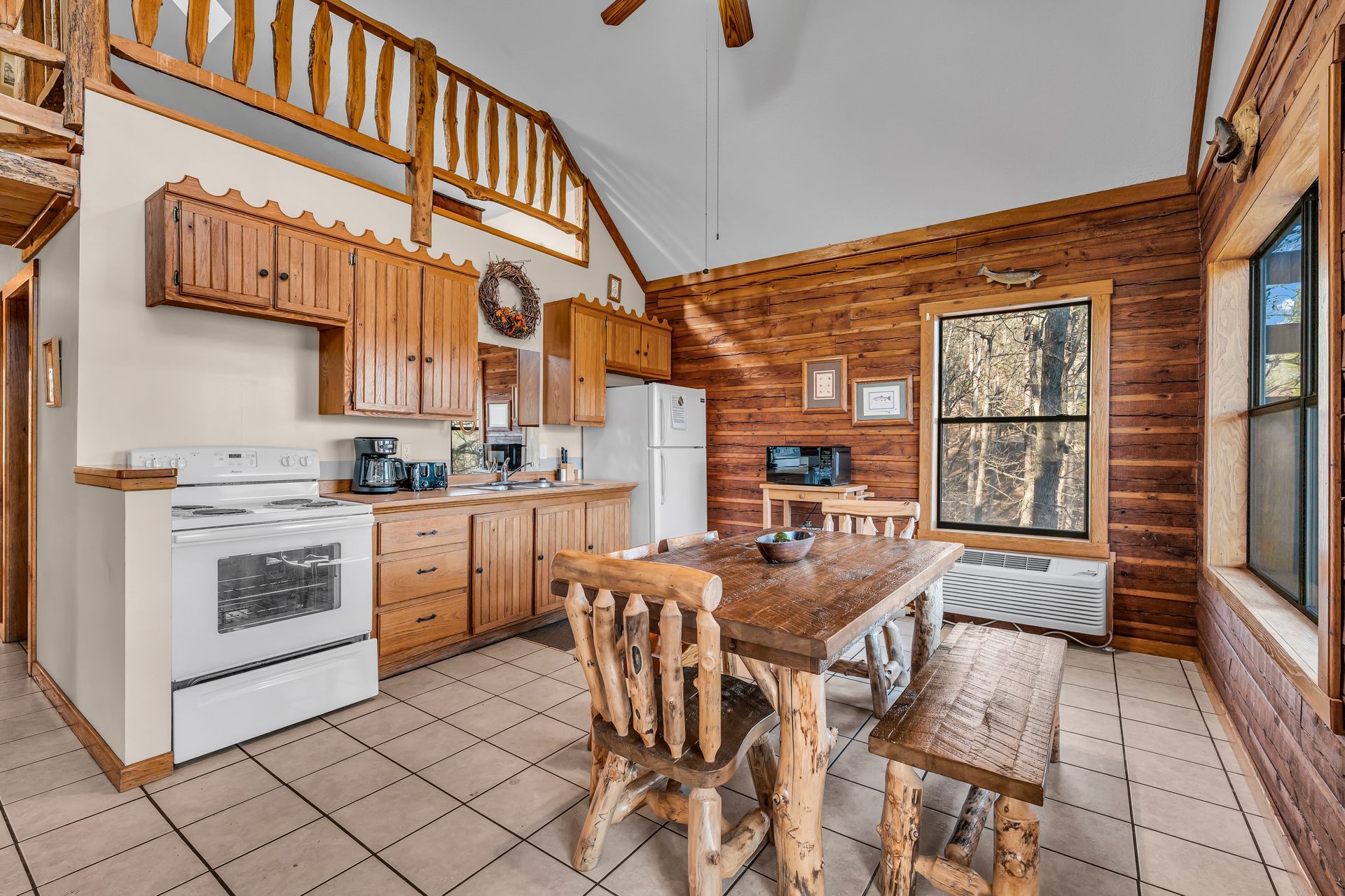 Rustic kitchen with wood cabinets, white appliances, dining table, and log cabin walls.
