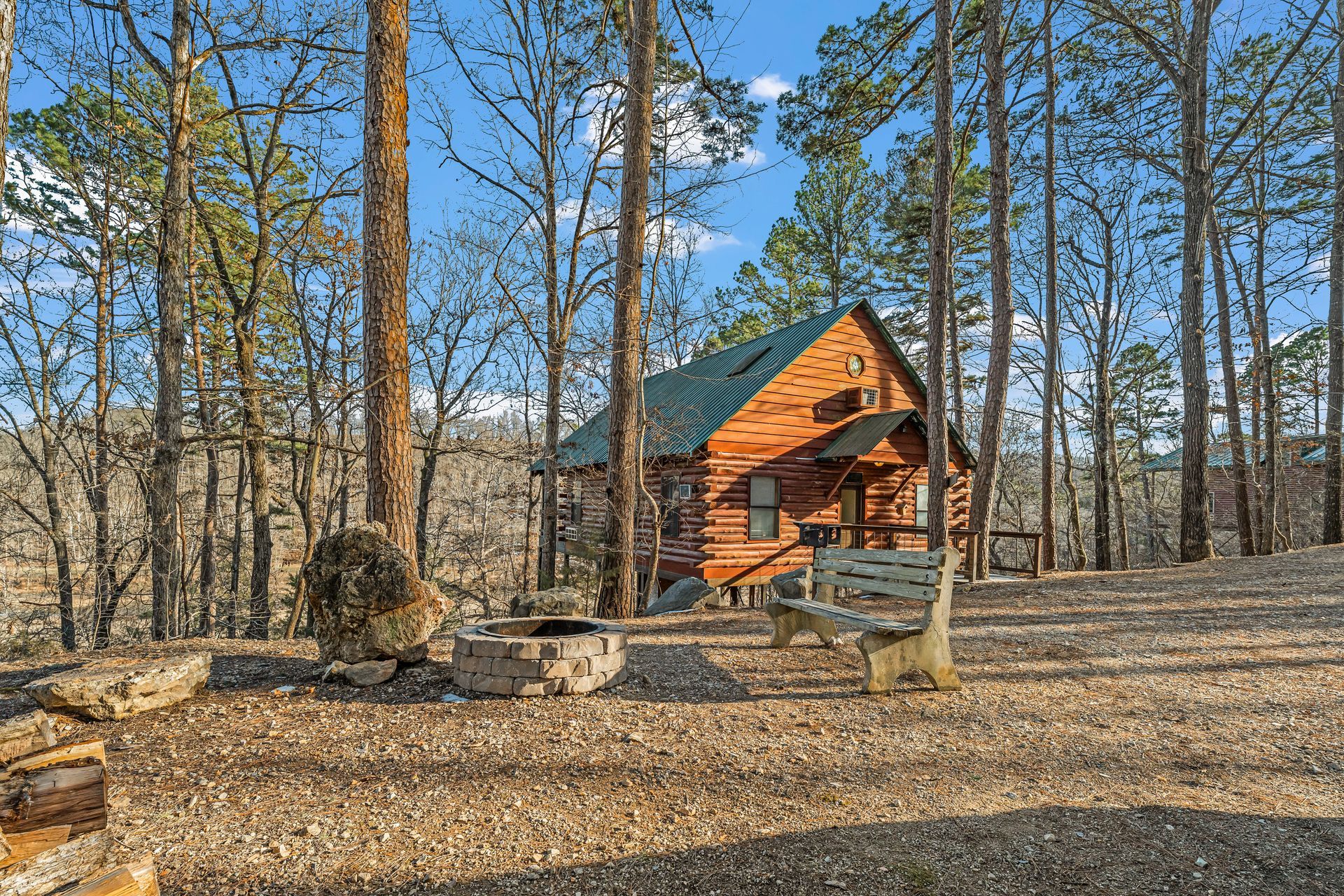 Small orange cabin in a wooded clearing beside a fire pit under a bright blue sky