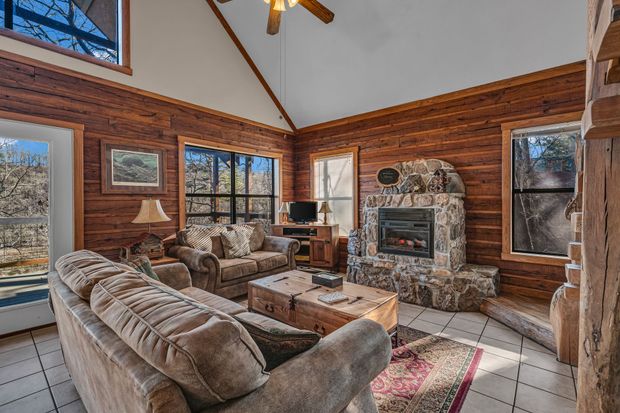 Cozy log cabin living room with stone fireplace, large windows, and plaid sofas