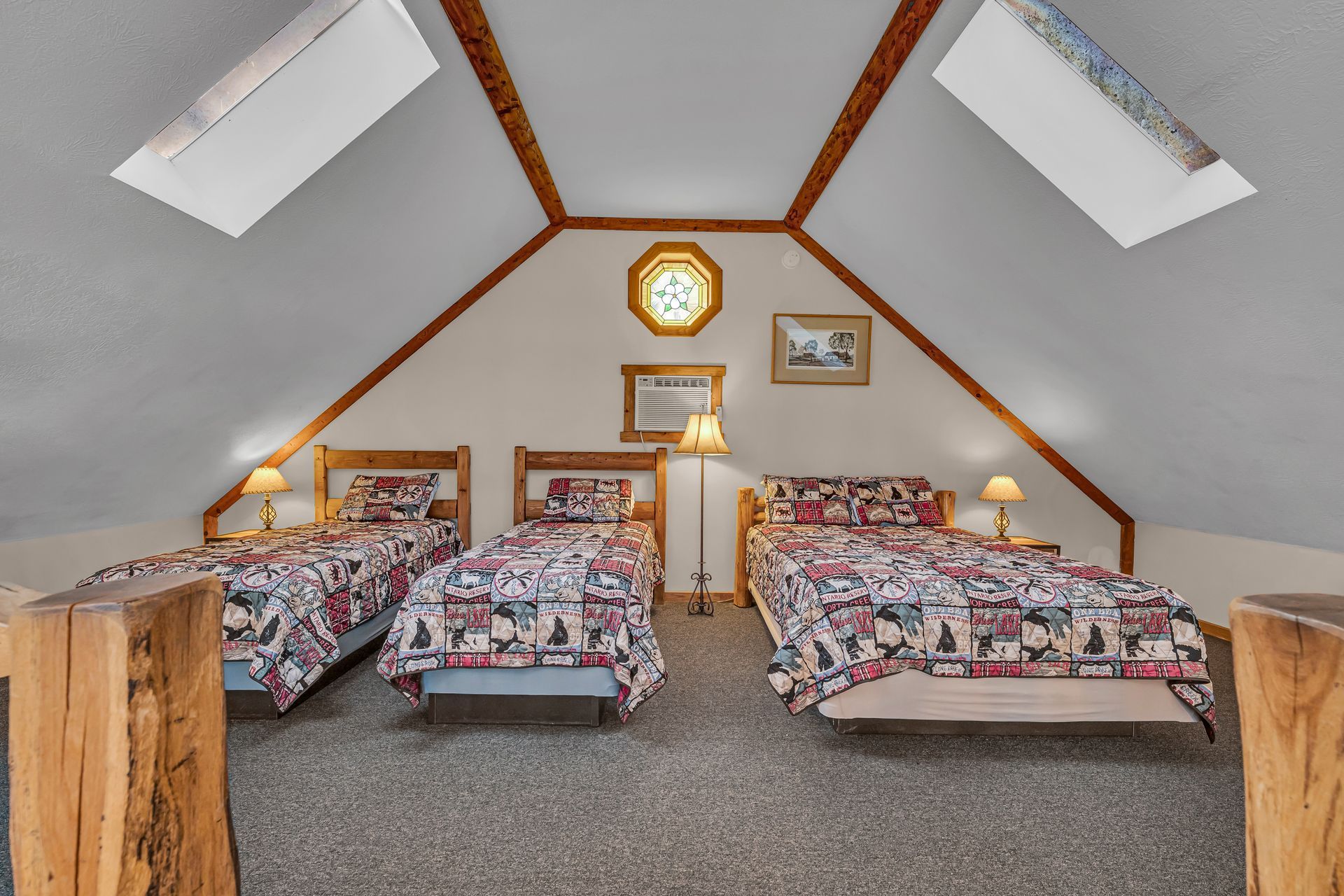 Attic bedroom with four twin beds, skylight windows, and a wooden-framed ceiling, warmly lit.