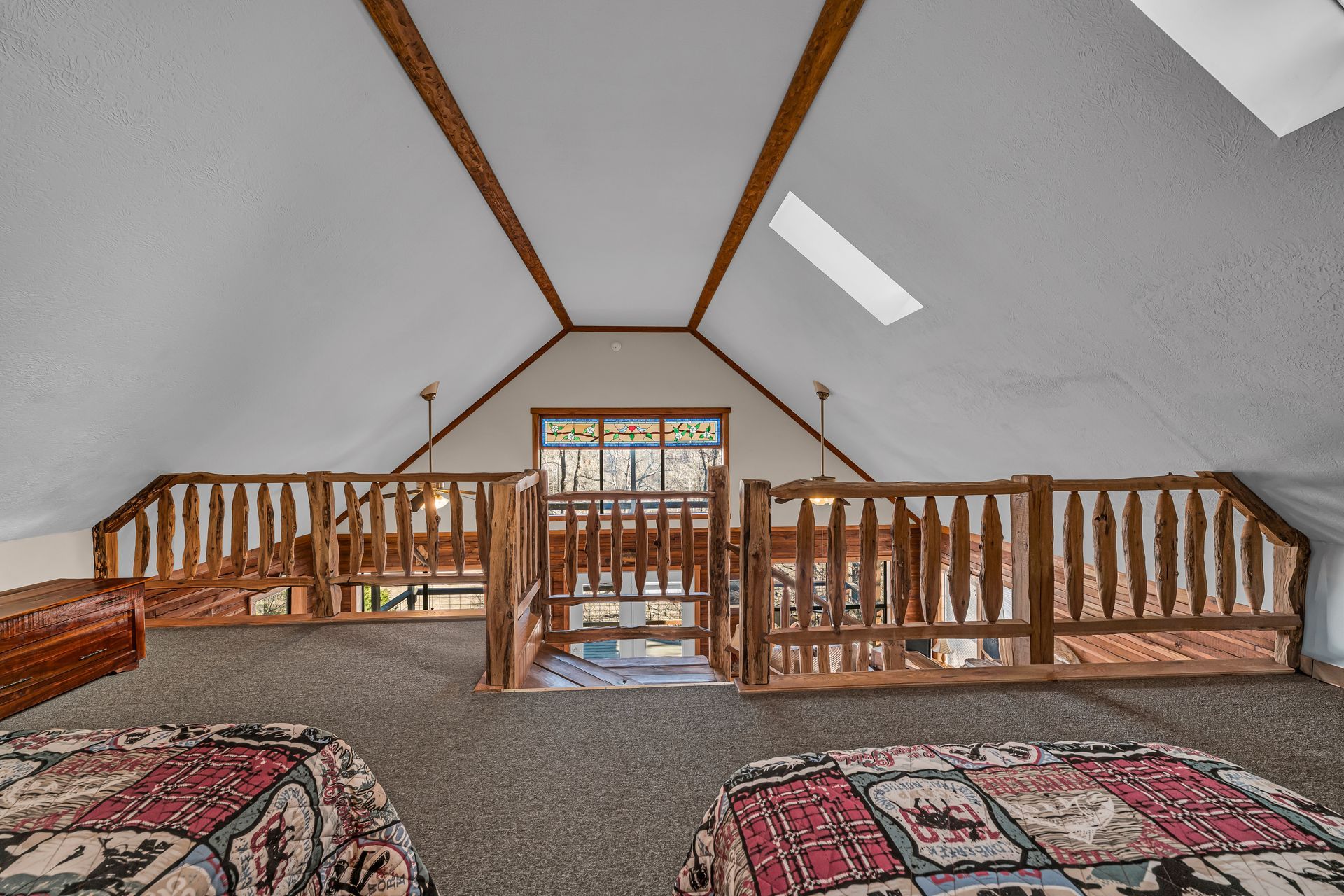 Attic loft with wooden railing, vaulted ceiling, skylight, and patterned rugs