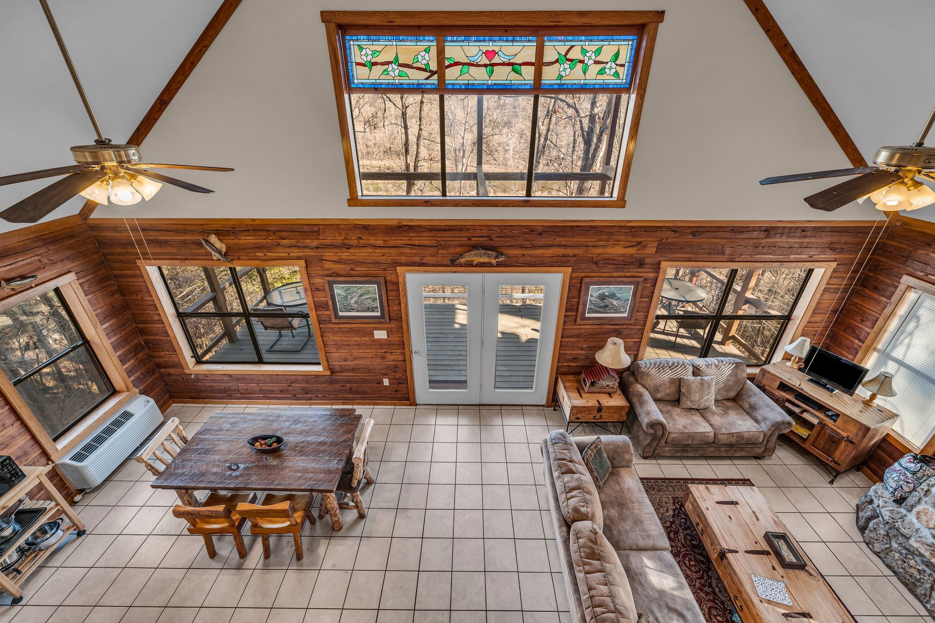 Cozy rustic living room with wood walls, large windows, skylight, and a sofa, table, and chairs.