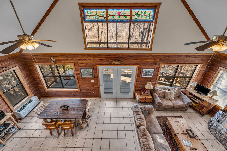 Rustic sunroom with wood walls, stained-glass skylight, gray seating, and a dining table beneath ceiling fans